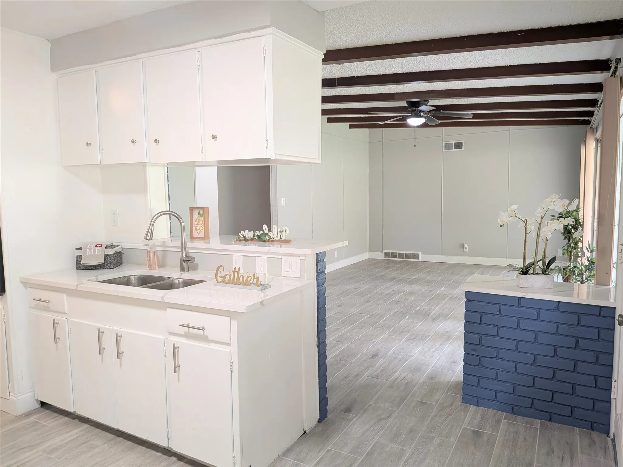 Kitchen featuring white cabinetry with silver-tone hardware, a dual-basin stainless steel sink, and light-toned countertops