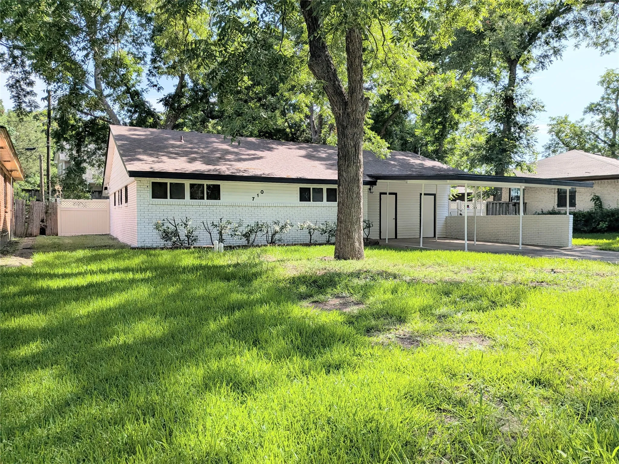 Single-story residence featuring a white painted brick exterior, a brown shingle roof, and a covered carport