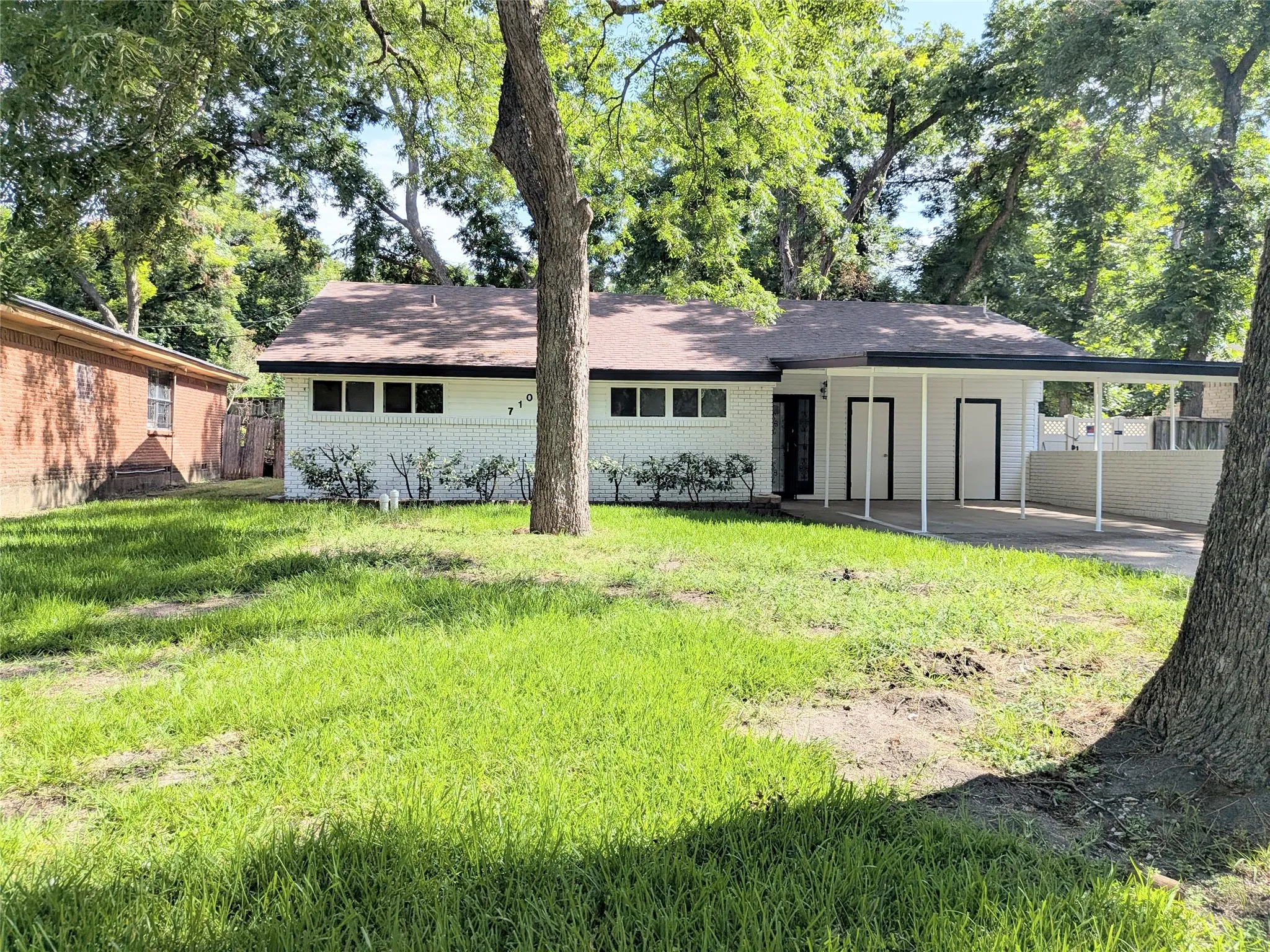 White brick exterior with a brown shingle roof, featuring a covered carport and a spacious front lawn