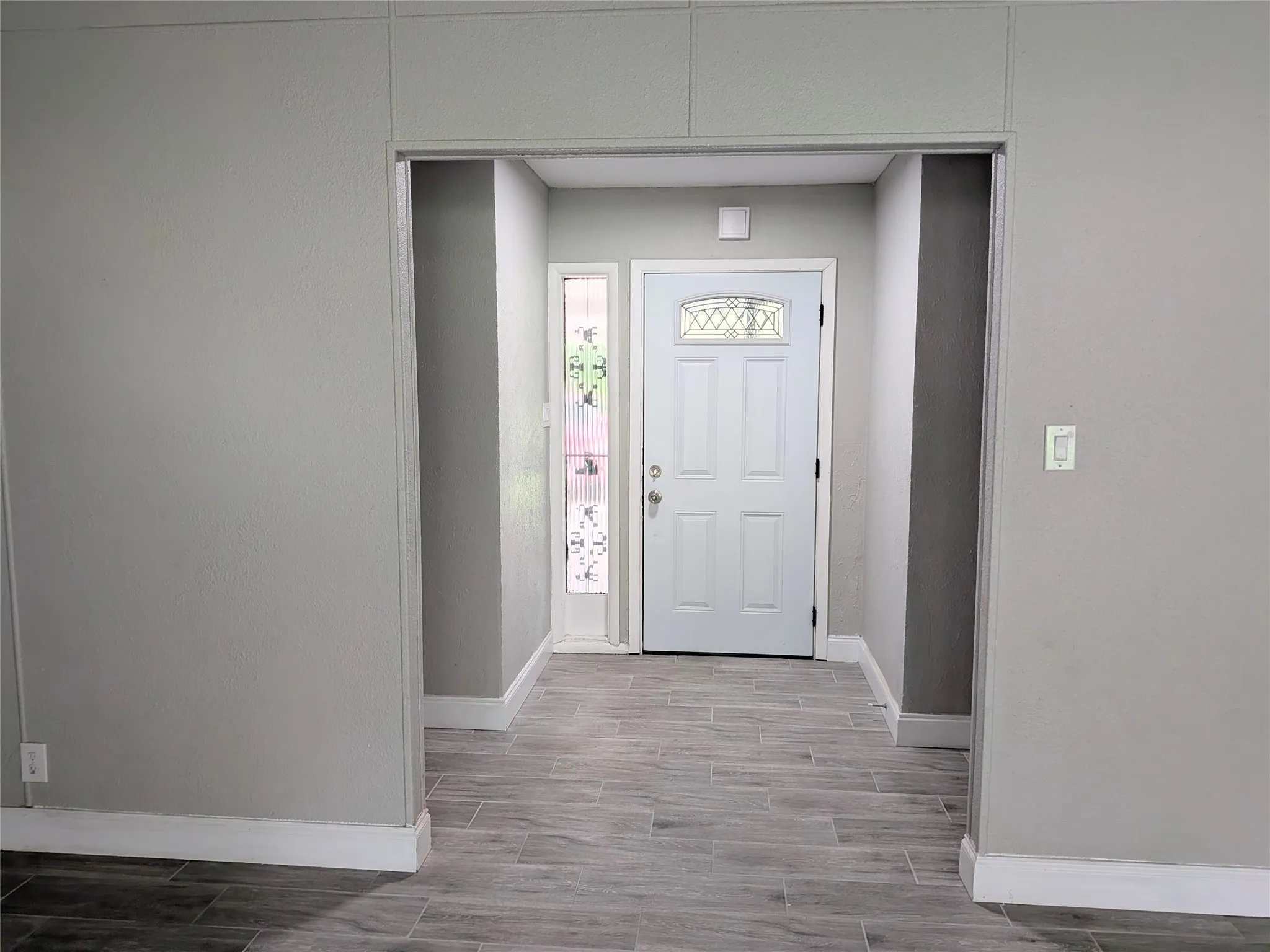 Entryway featuring a decorative glass panel door, side light, wood-finish tile flooring, and neutral wall tones