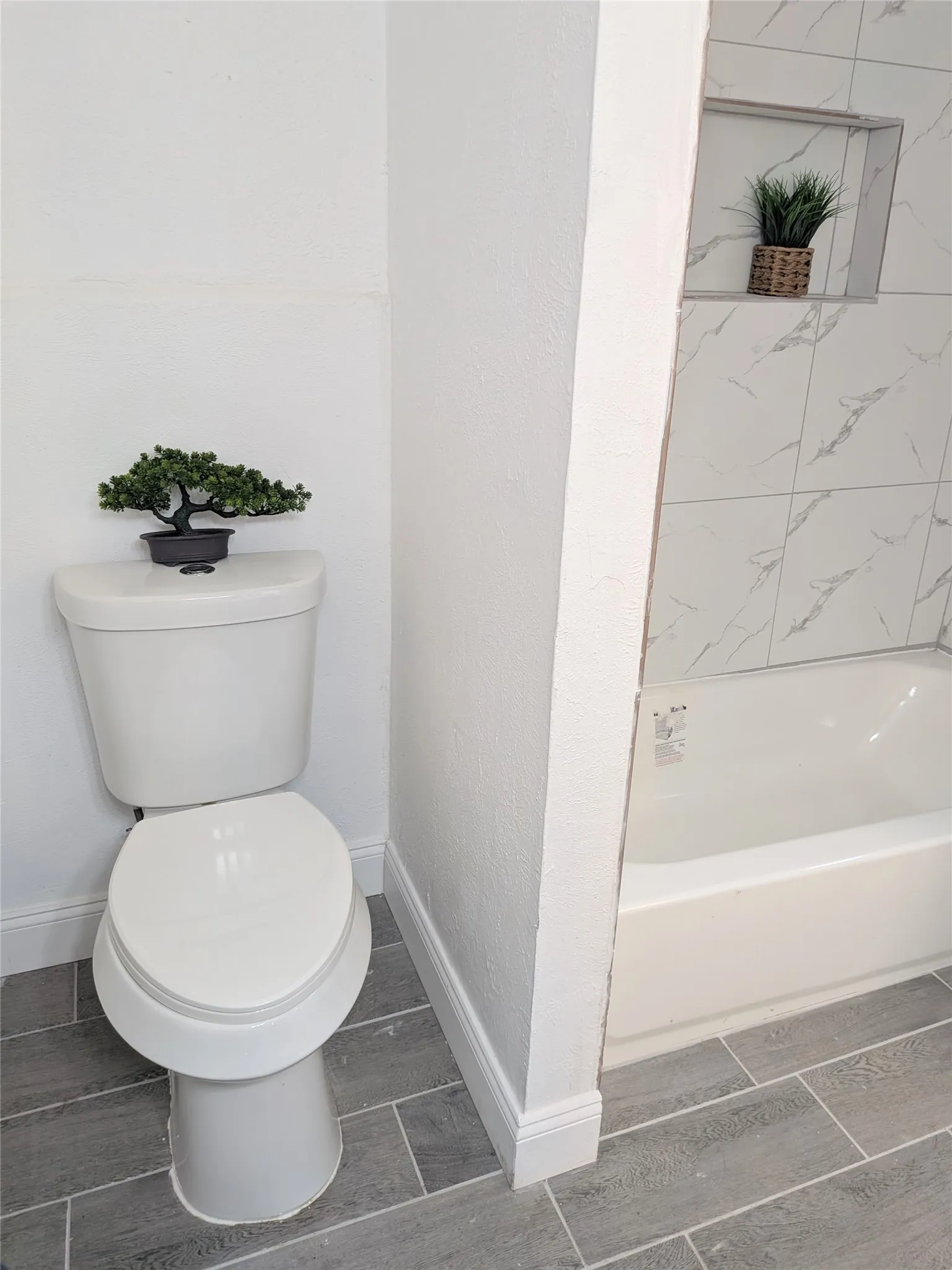 Full bathroom featuring a white porcelain toilet, a white bathtub, and contemporary gray tile flooring