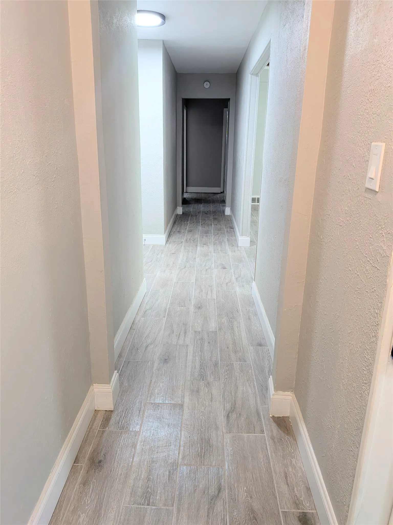 Hallway featuring wood-finish tile flooring, recessed lighting, neutral wall tones, and white baseboards