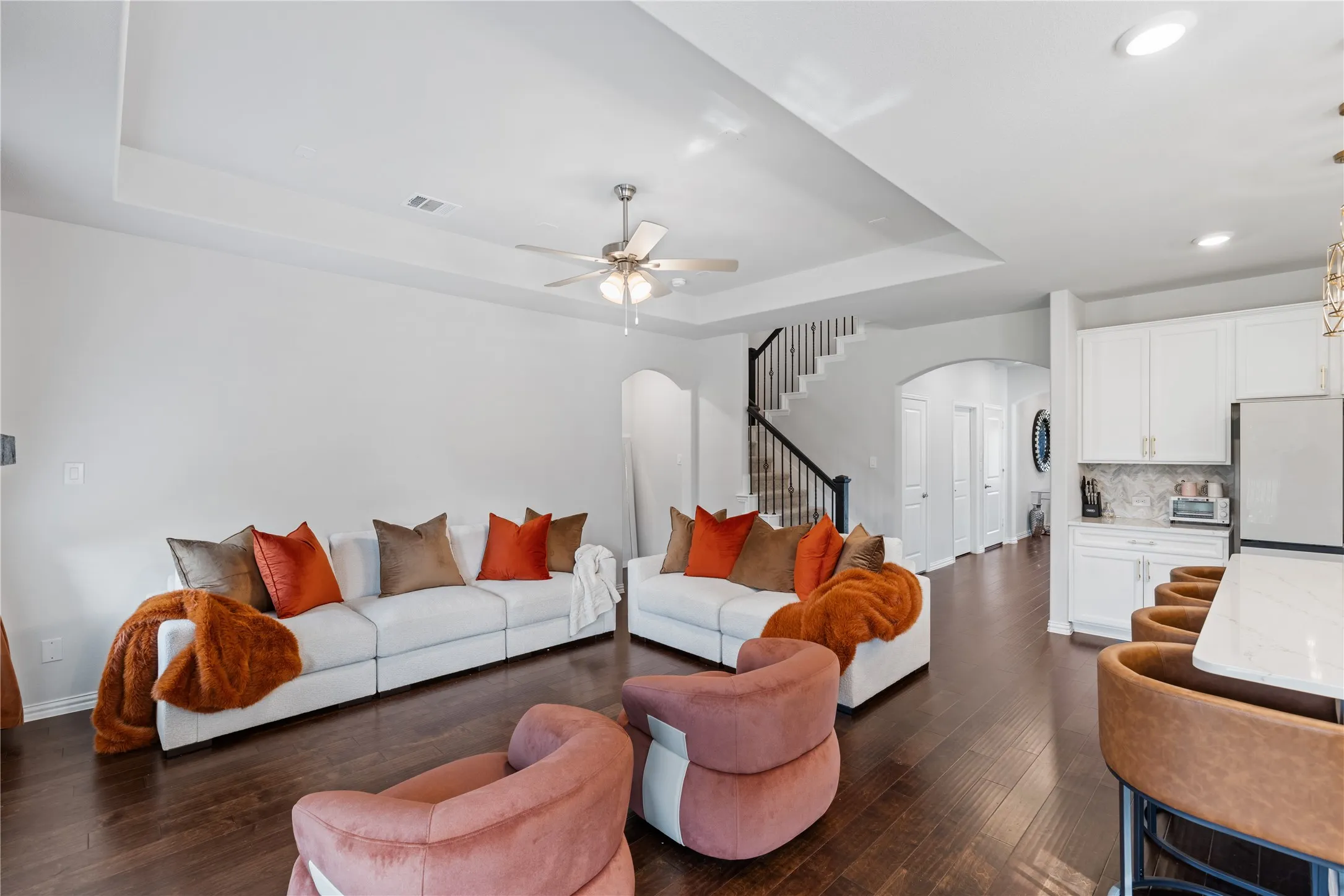 Spacious open-concept family room featuring rich upgraded flooring, soaring tray ceilings, designer lighting, and an elegant open staircase with wrought iron balusters. The seamless flow into the gourmet kitchen creates the perfect layout for entertaining and everyday living.