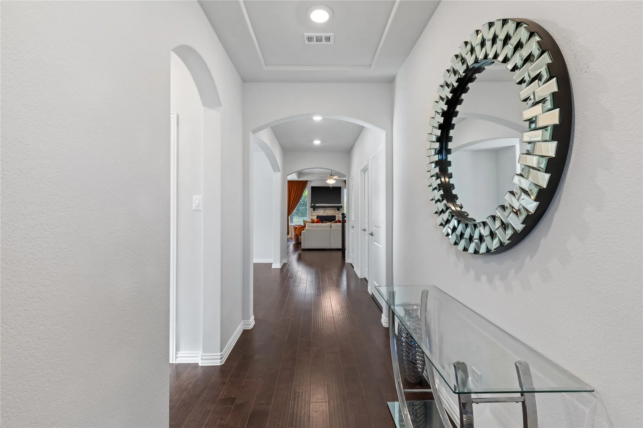 Hallway featuring wood-finish flooring, recessed lighting, and arched doorways. Step inside to soaring ceilings, rich hardwood flooring, elegant tray ceiling, decorative archways, recessed lighting, and an open-concept design that creates an impressive first impression.