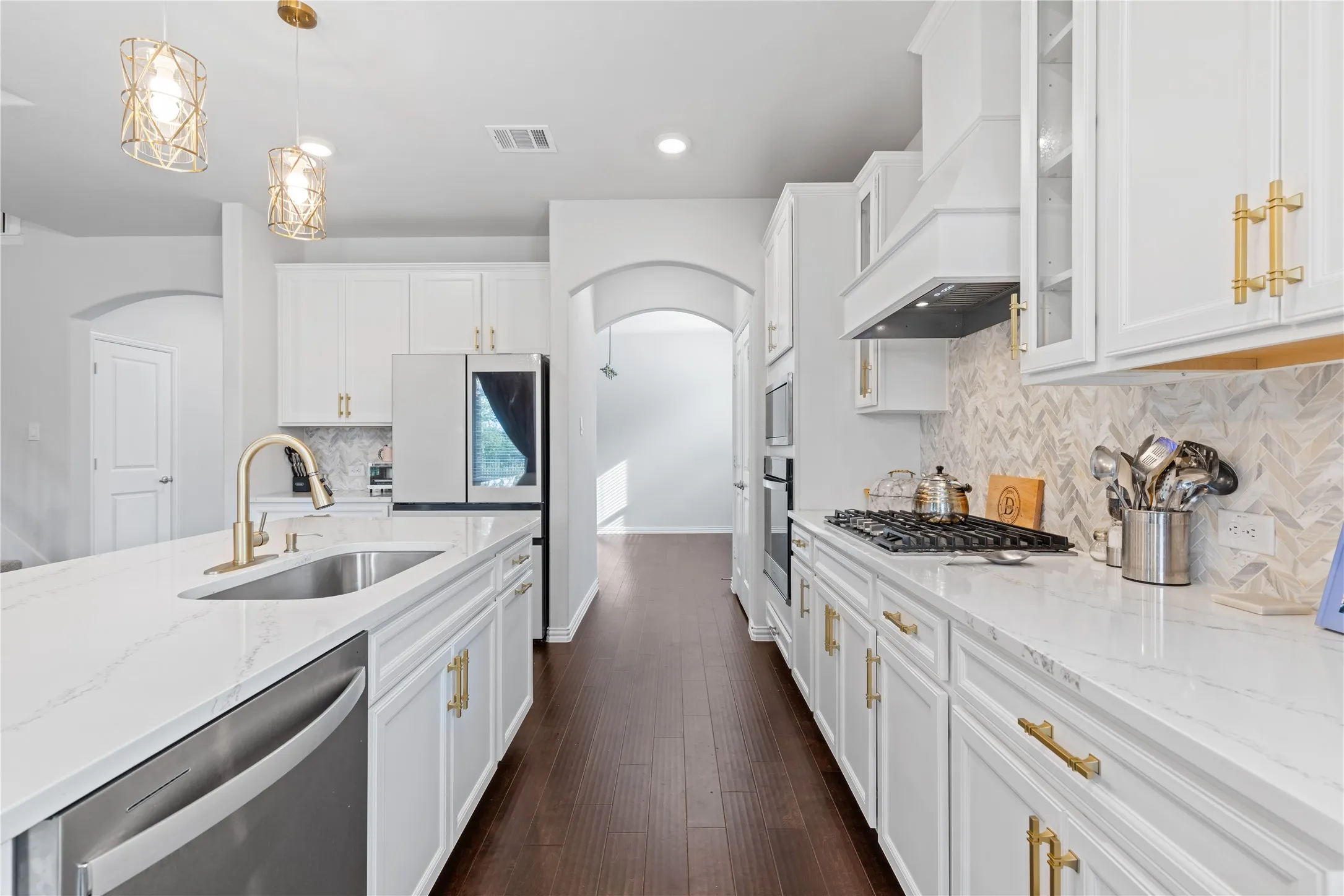 Beautiful chef’s kitchen showcasing expansive quartz countertops, upgraded cabinetry, decorative vent hood, premium appliances, walk-in pantry, custom hardware, and elegant designer finishes throughout.