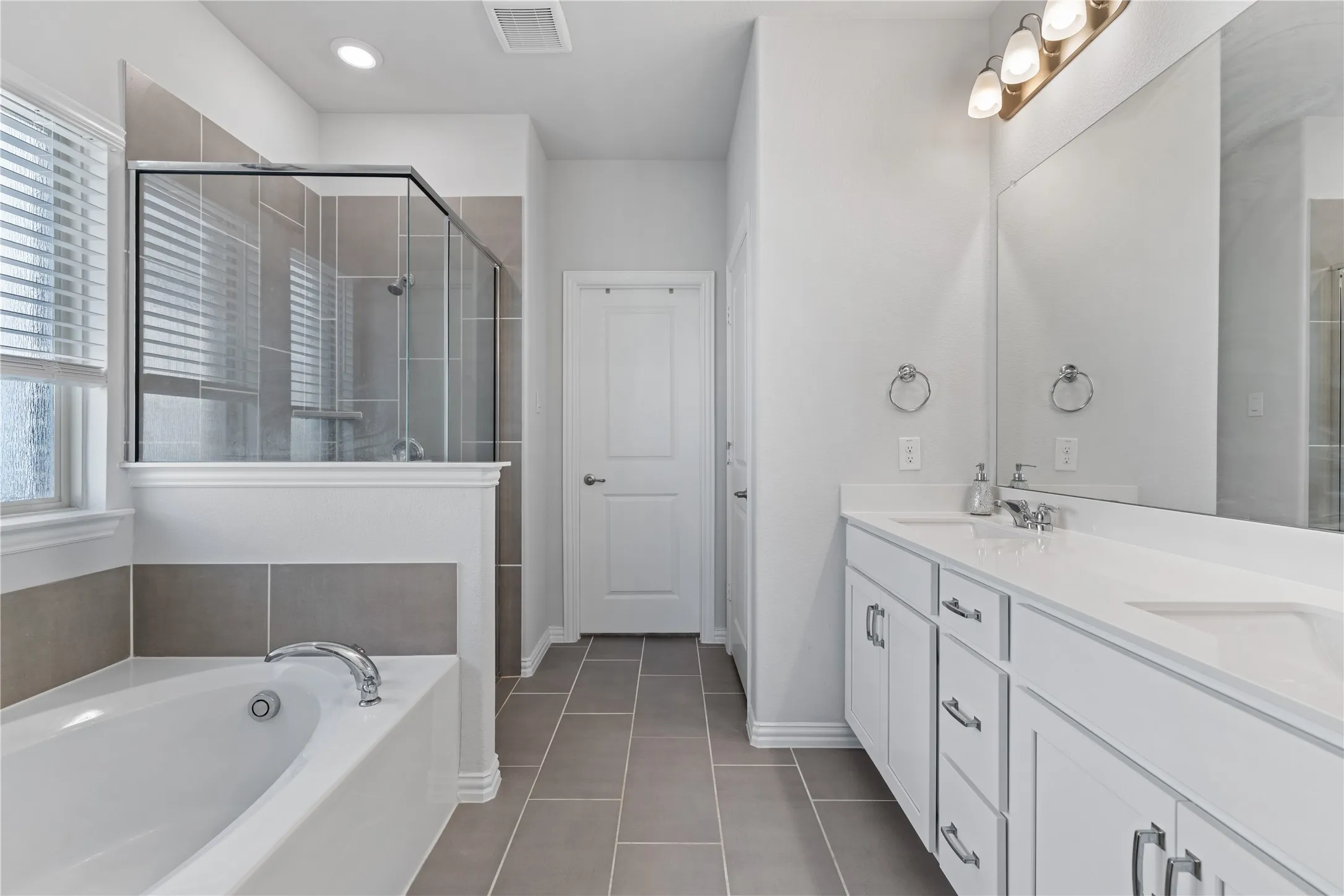 Spa-inspired primary bathroom featuring dual vanities, oversized framed mirrors, soaking garden tub, oversized walk-in shower with glass enclosure, designer tile, and spacious linen storage.