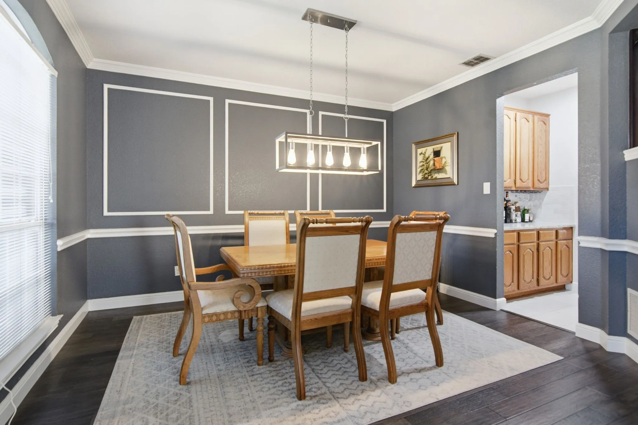 Dining room featuring dark wood-finish flooring, wainscoting with decorative trim, a modern linear chandelier, and an arched entry