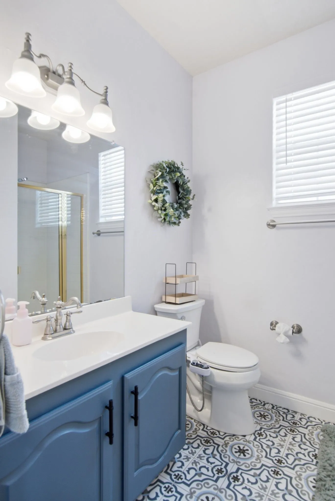 Downstairs full bathroom with walk-in shower featuring decorative floor tiling, a single vanity with a blue cabinet and white countertop