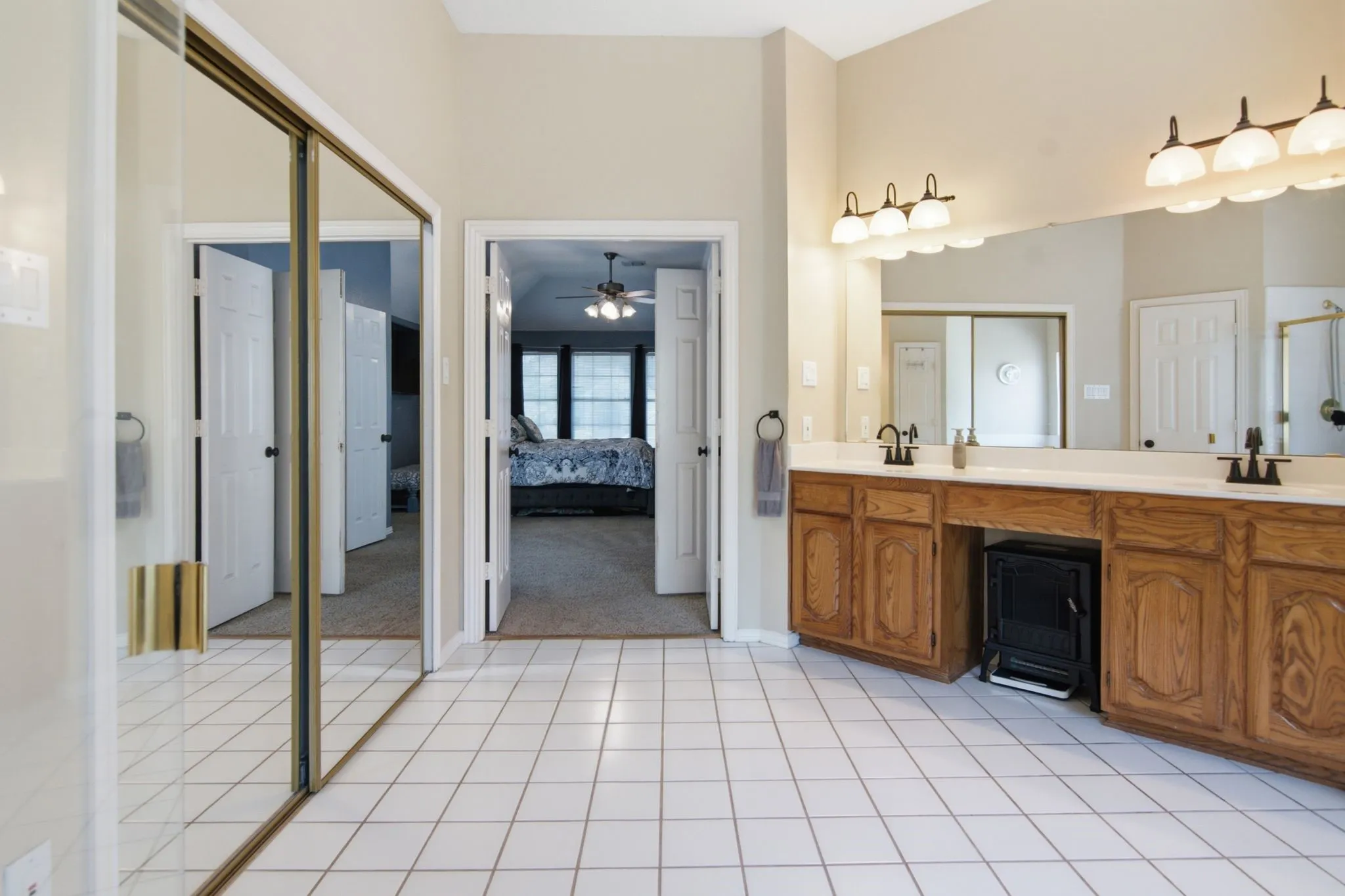 White tile flooring in this bathroom featuring a double vanity with wood cabinetry and a large mirror