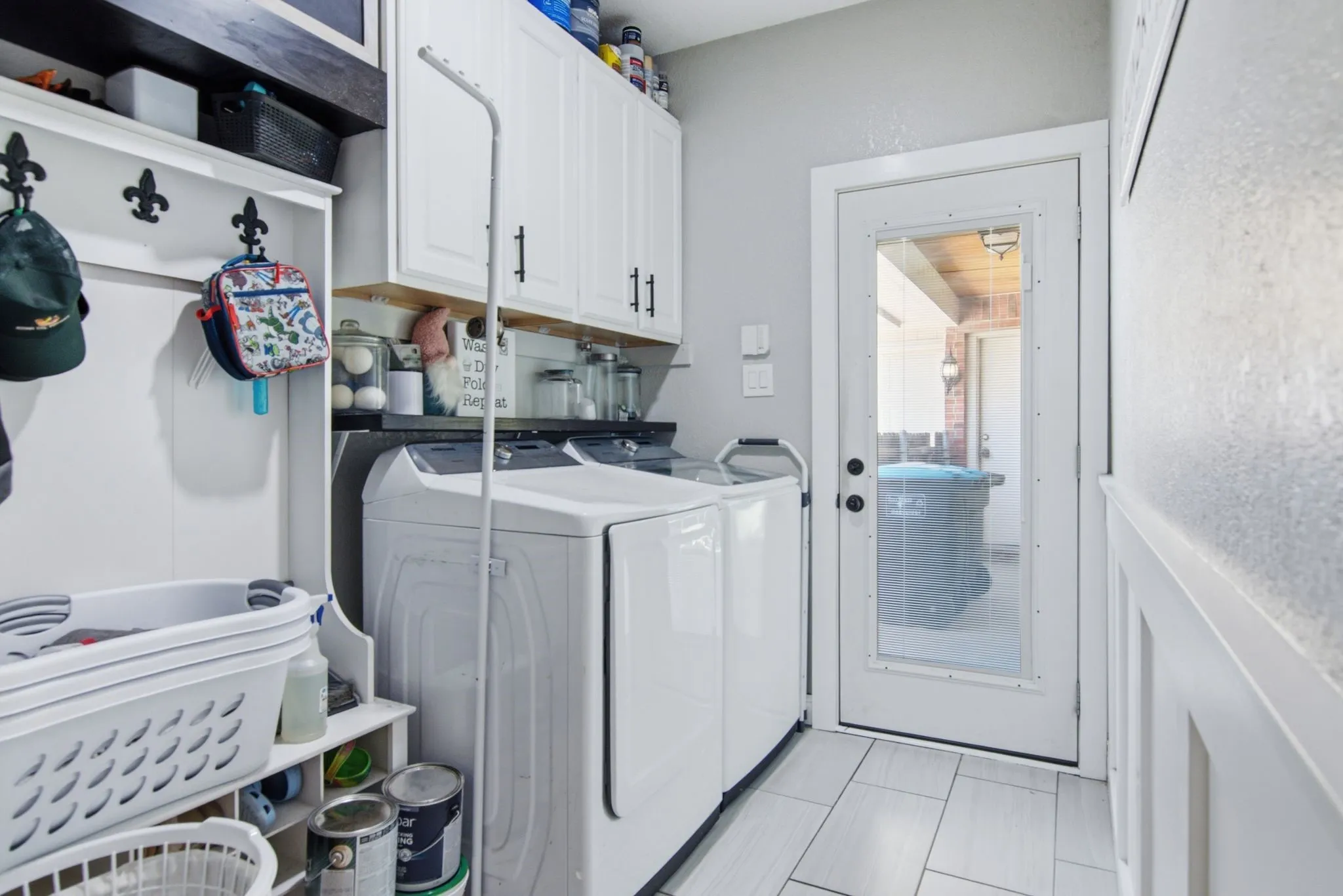 Utility area featuring white shaker-style cabinetry, tile flooring and a glass-paneled exterior door.