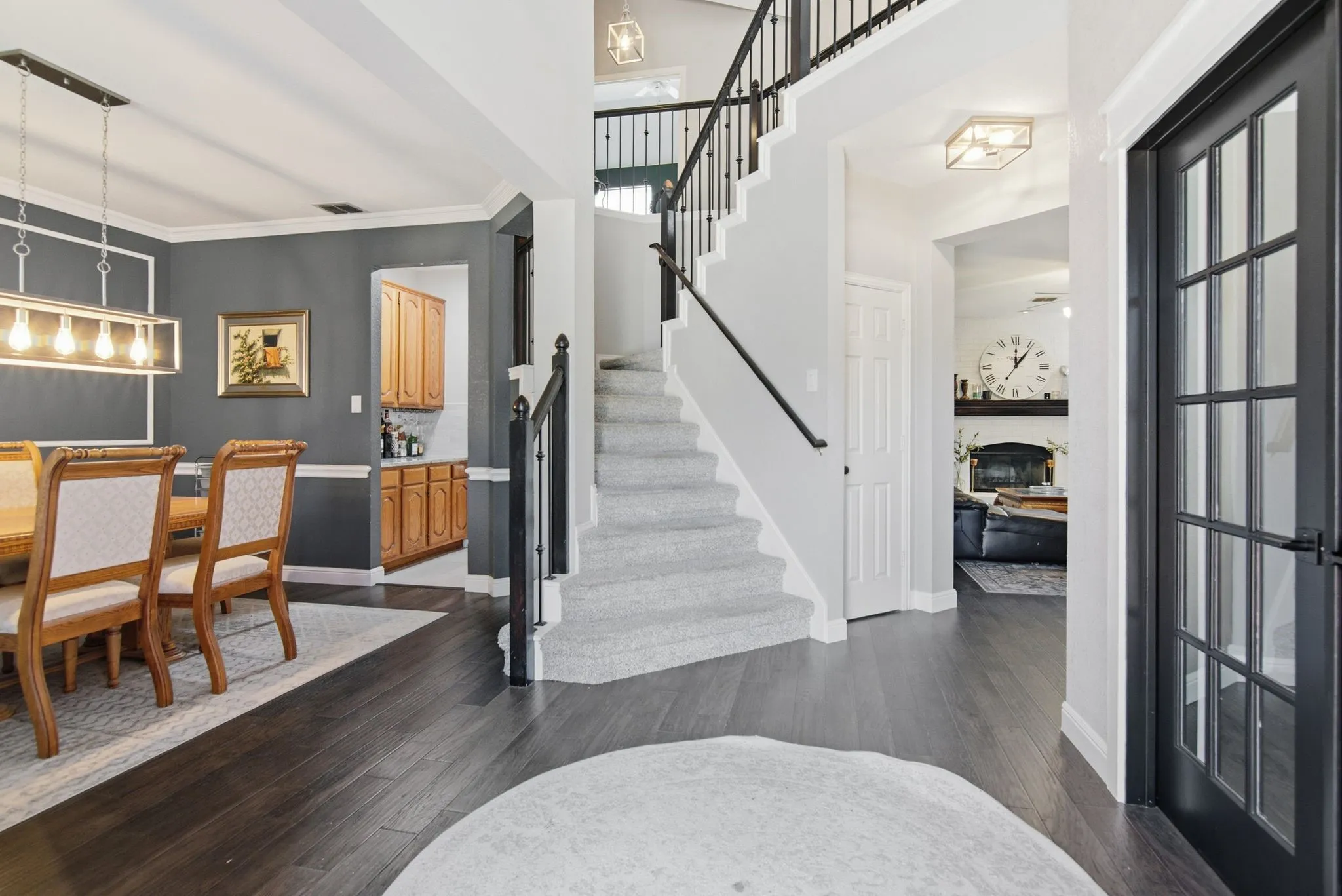 Spacious entryway featuring dark wood-finish flooring, a carpeted staircase with dark iron balusters, a glass-paneled door leading to the living room/office area.