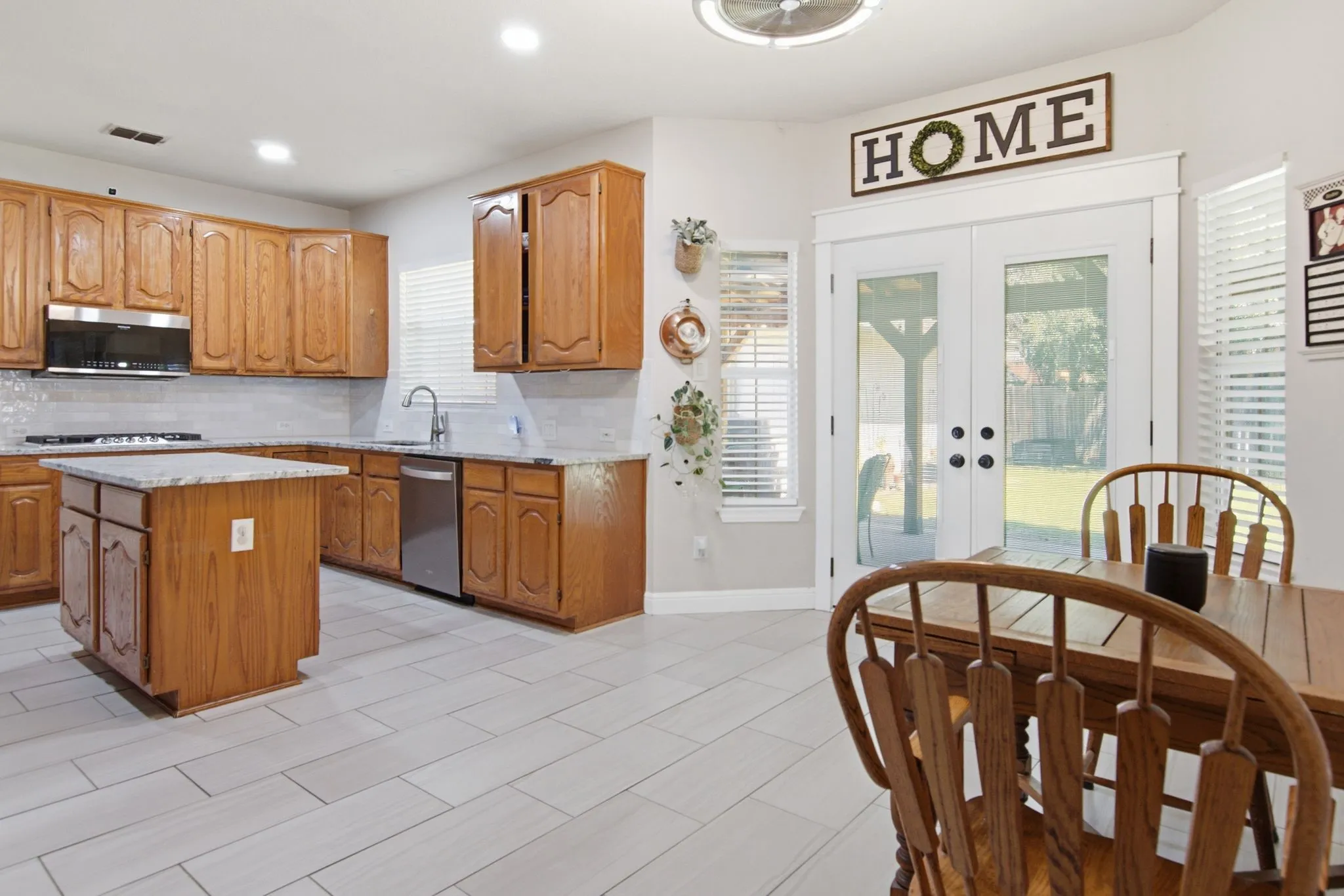 Kitchen featuring wood cabinetry, granite countertops, stainless steel appliances, a center island, and light plank tile flooring
