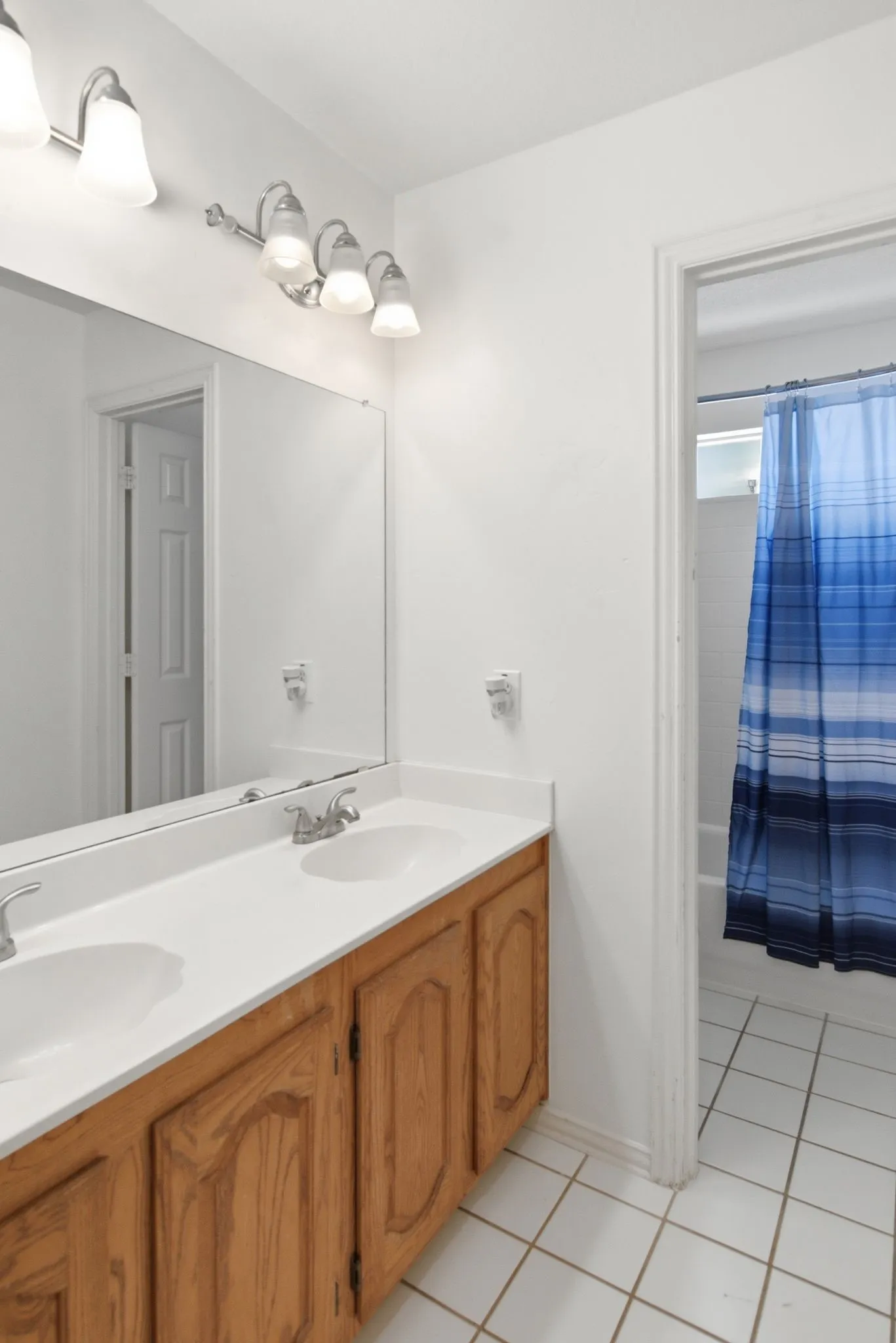 Bathroom featuring a dual vanity with a white countertop and wood-finish cabinetry. Full tub/shower separate from vanities.