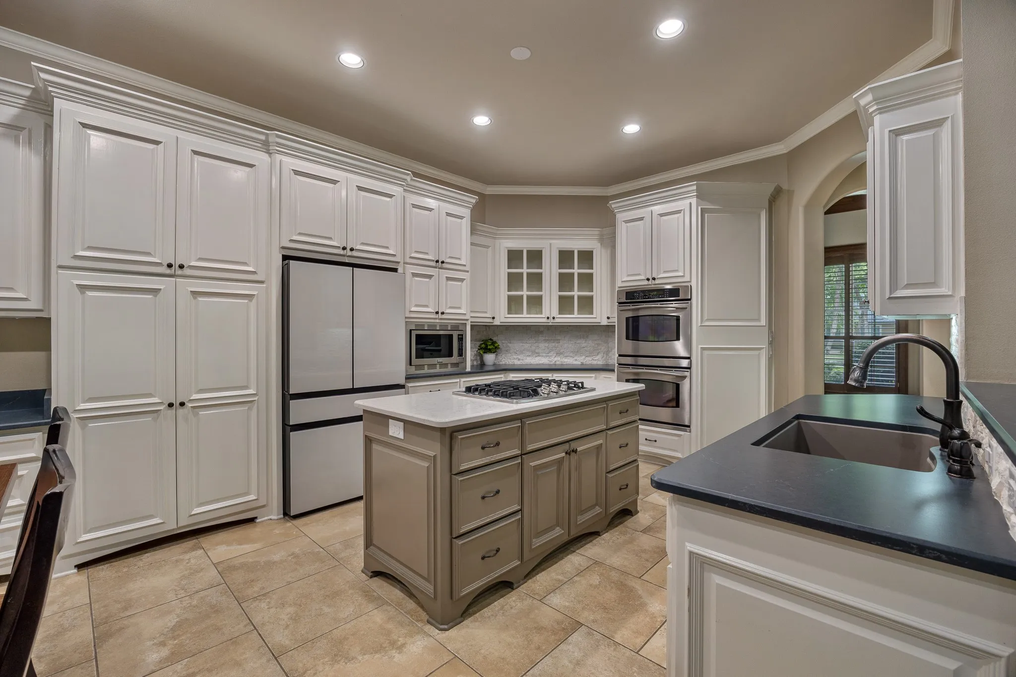 Spacious kitchen featuring white cabinetry, a center island with a gas cooktop, stainless steel appliances, dark countertops, and tiled flooring