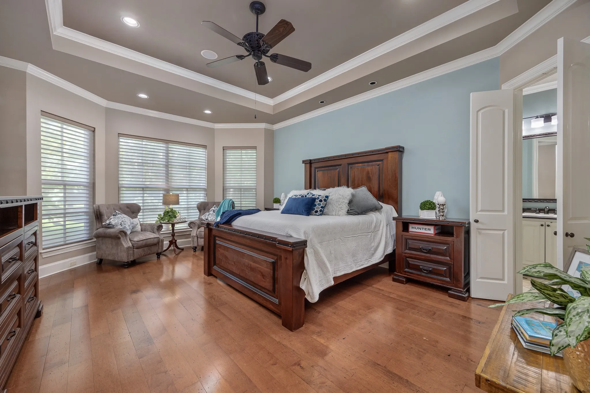 Spacious room featuring wood flooring, a tray ceiling with recessed lighting and a ceiling fan, and a large bay window with window treatments