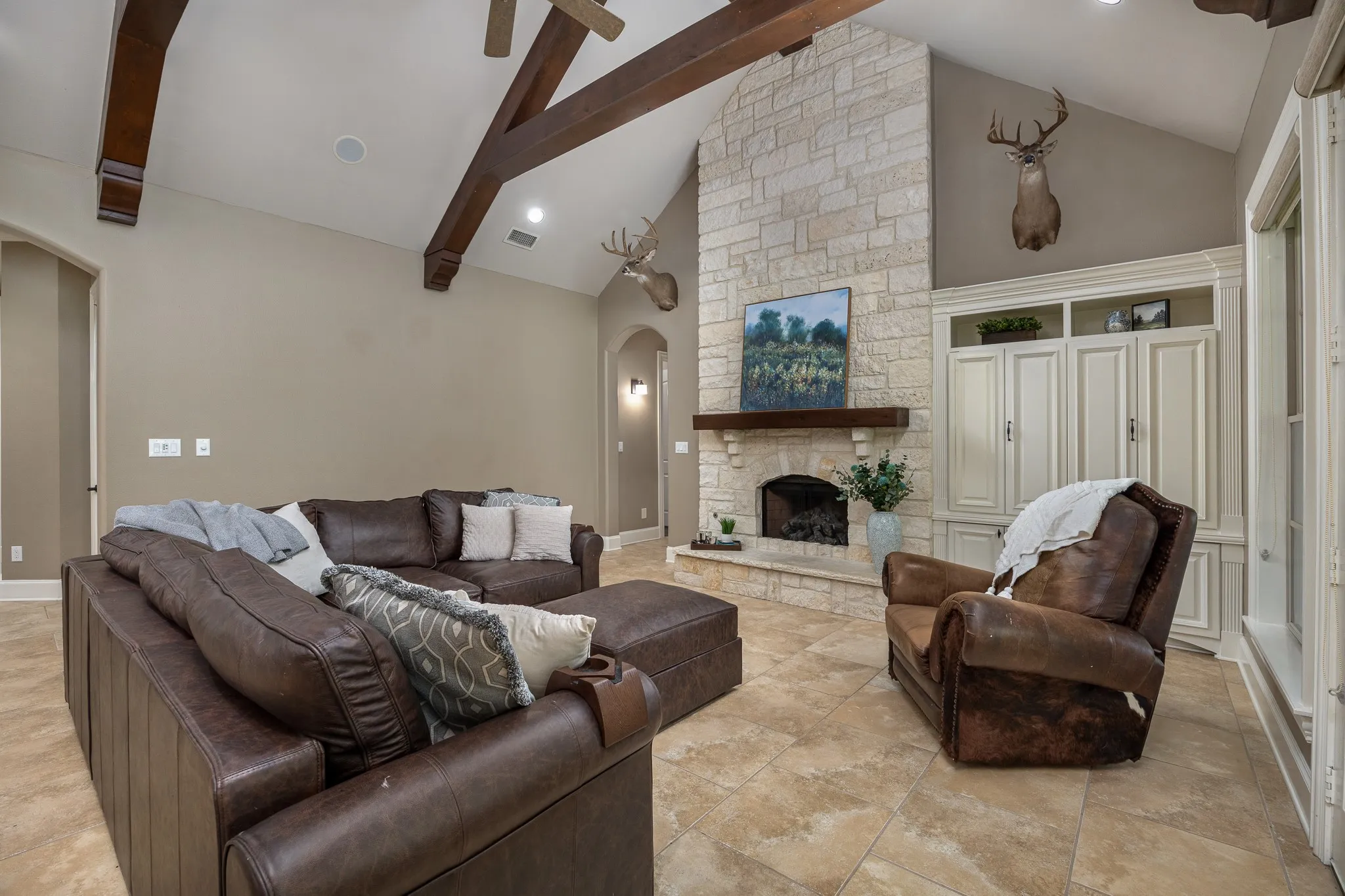 Vaulted ceiling with exposed wood beams, stone fireplace, built-in cabinetry, arched doorways, and tile flooring