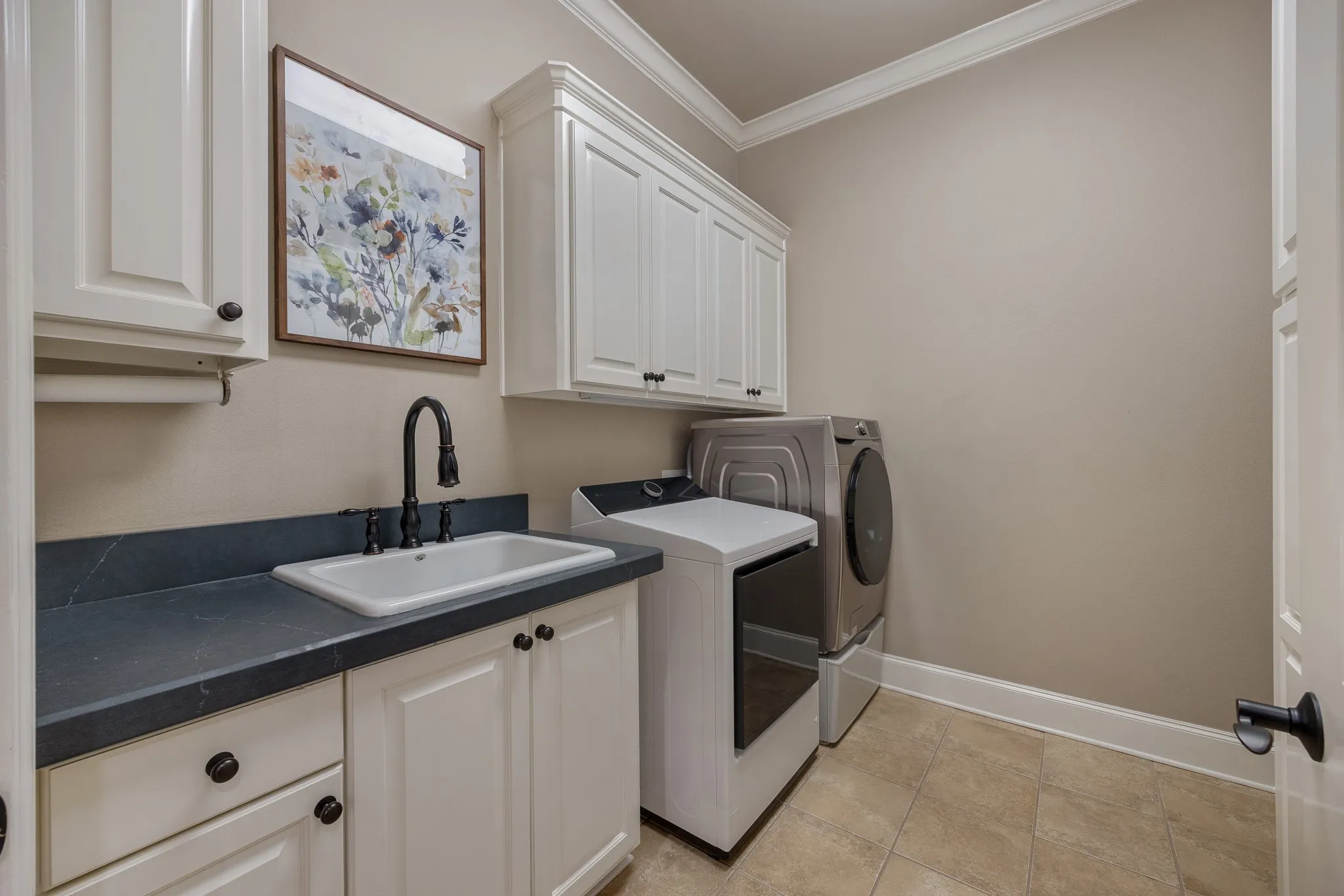Utility room featuring a built-in sink, white cabinetry with dark hardware, dark countertop, and crown molding