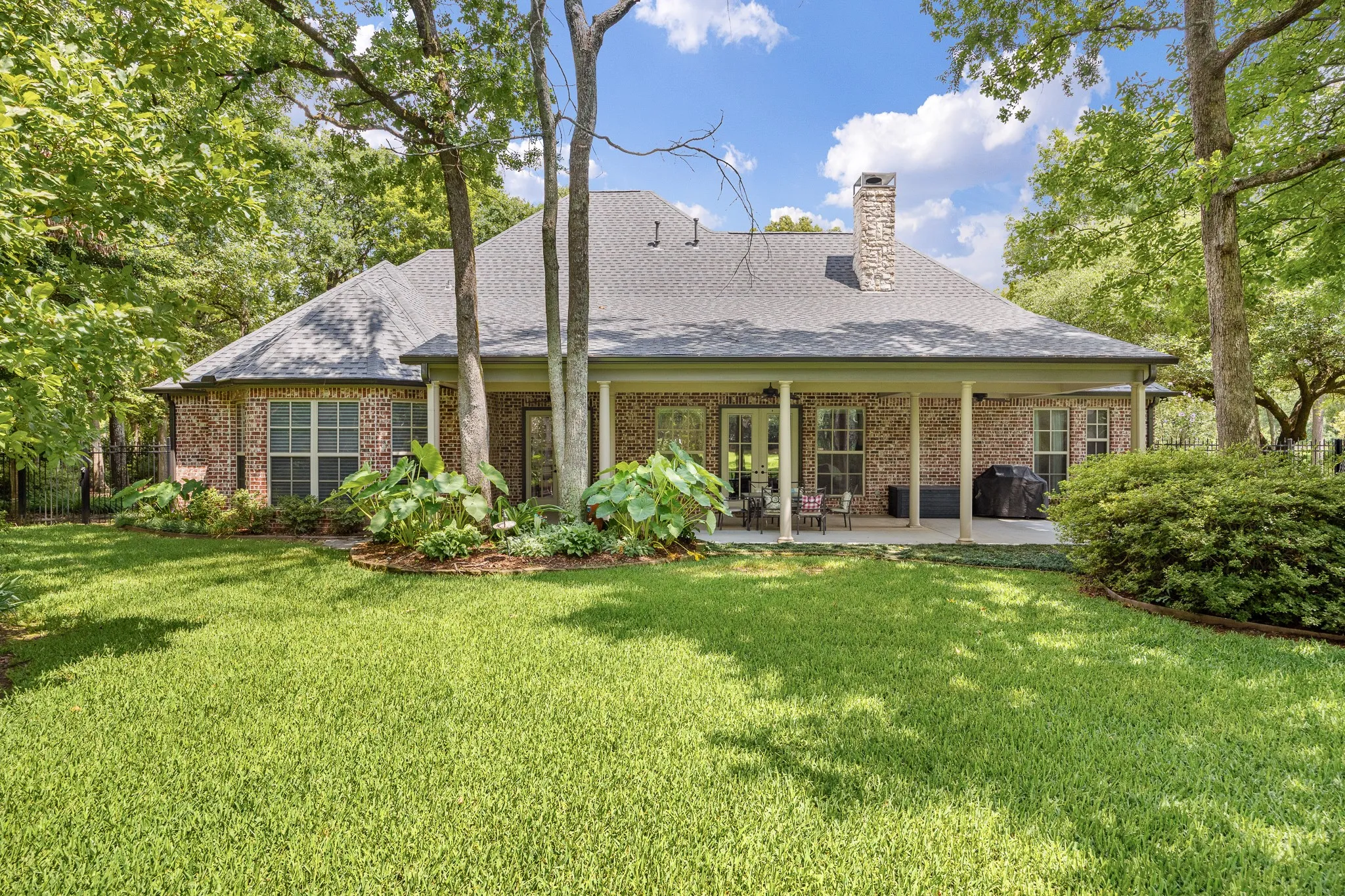 Expansive backyard featuring a manicured lawn, mature trees, and a covered patio