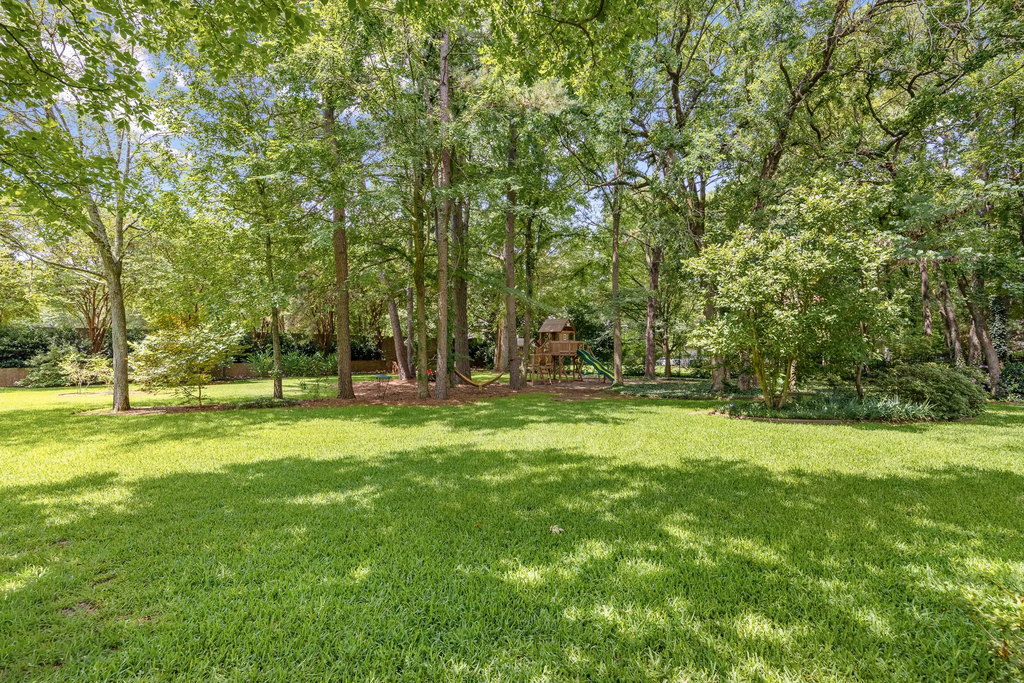 Expansive backyard featuring a lush lawn, mature trees providing natural shade, and dense perimeter landscaping