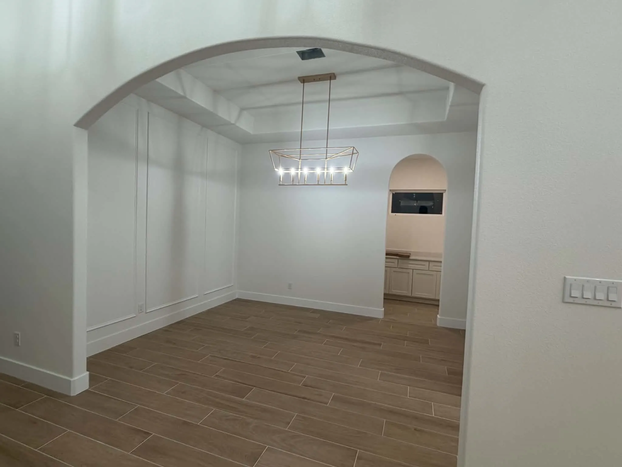 Archway entry to a room featuring wood-finish tile flooring, decorative wall paneling, a tray ceiling, and an architectural light fixture