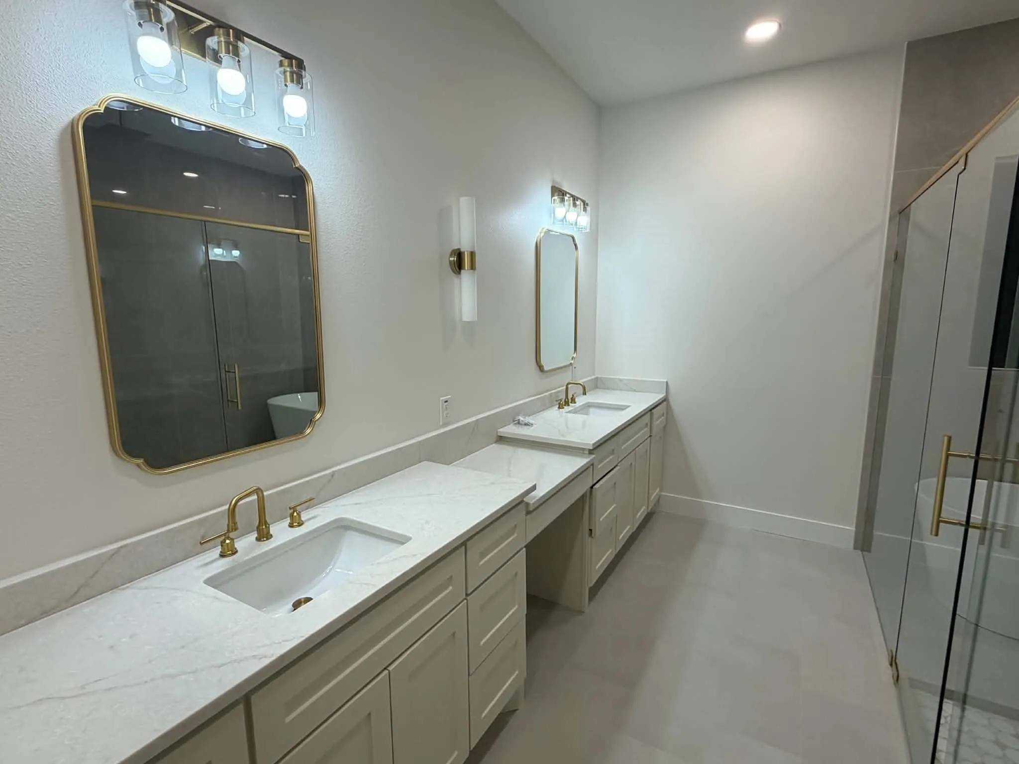 Dual vanity with integrated sinks, light-toned cabinetry, and gold-finish fixtures