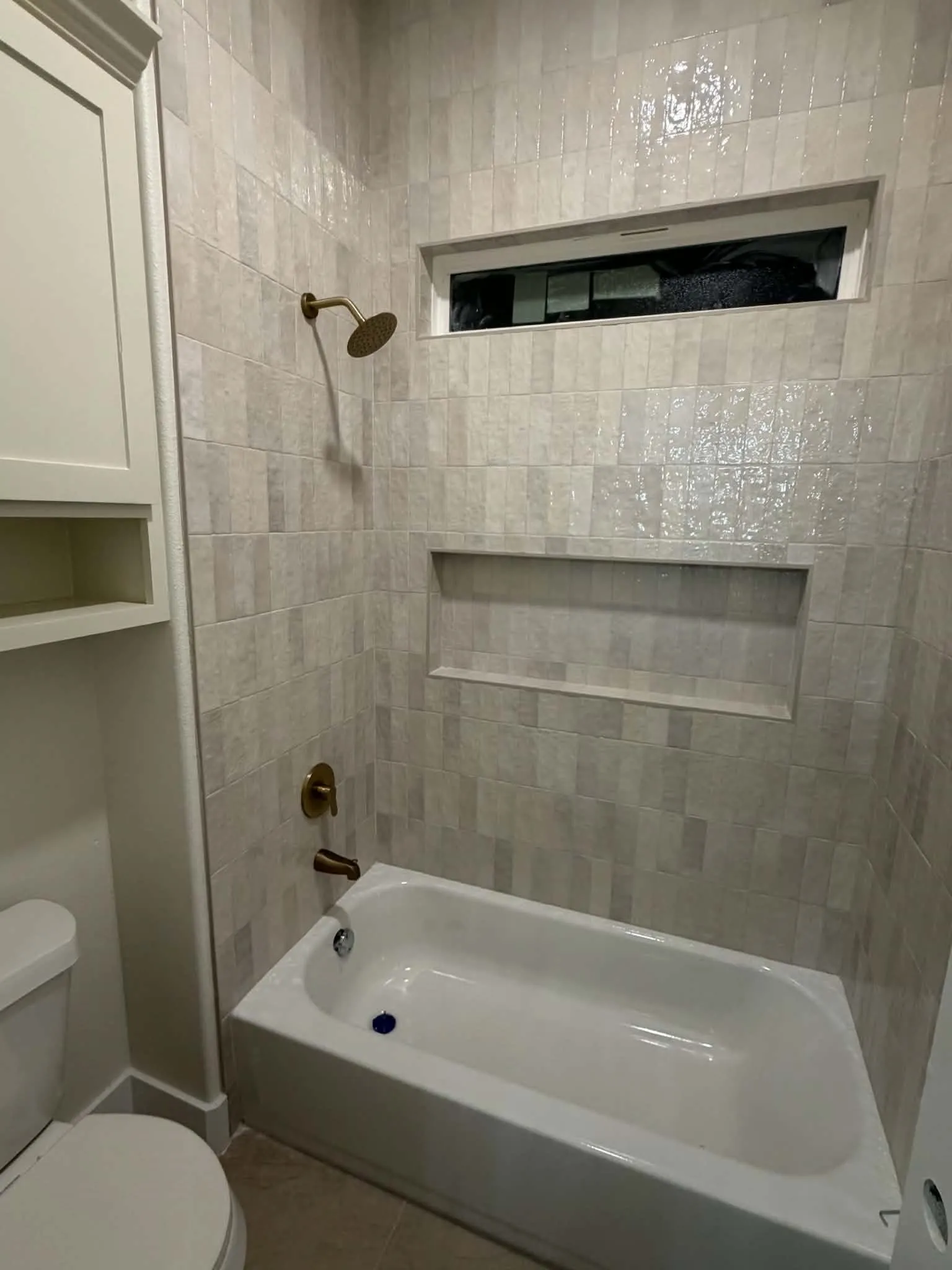 Bathtub with bronze-finish fixtures, a tiled shower surround, and a recessed niche