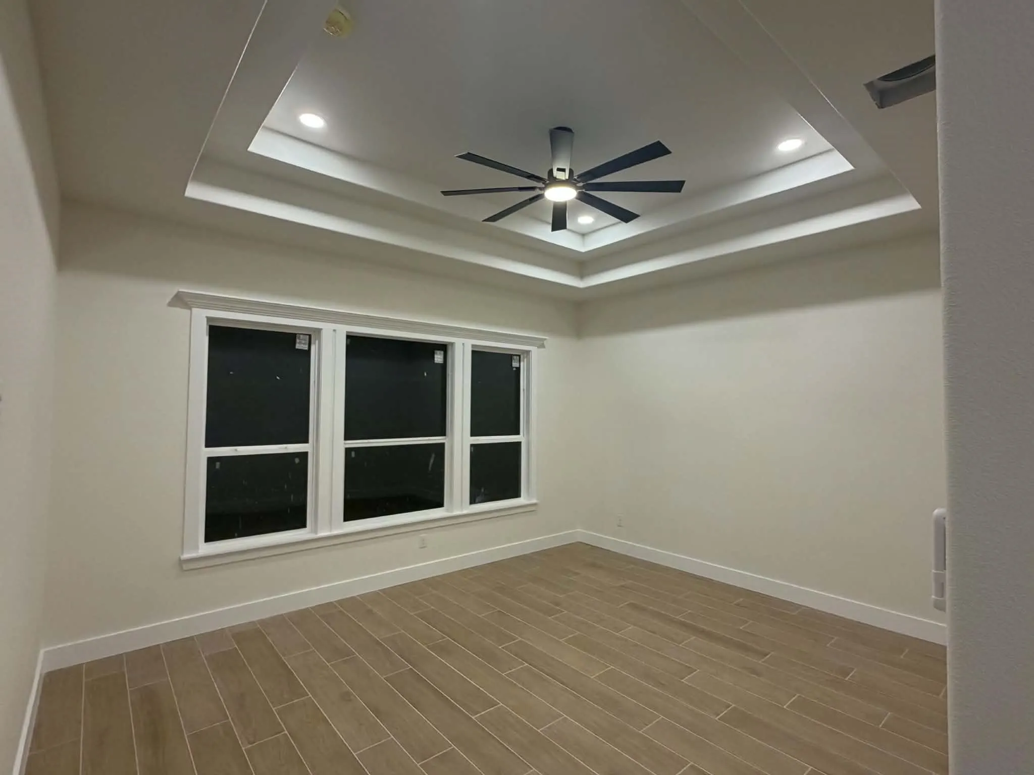 Tray ceiling with recessed lighting and a ceiling fan, wall-to-wall windows with white trim, and wood-finish tile flooring