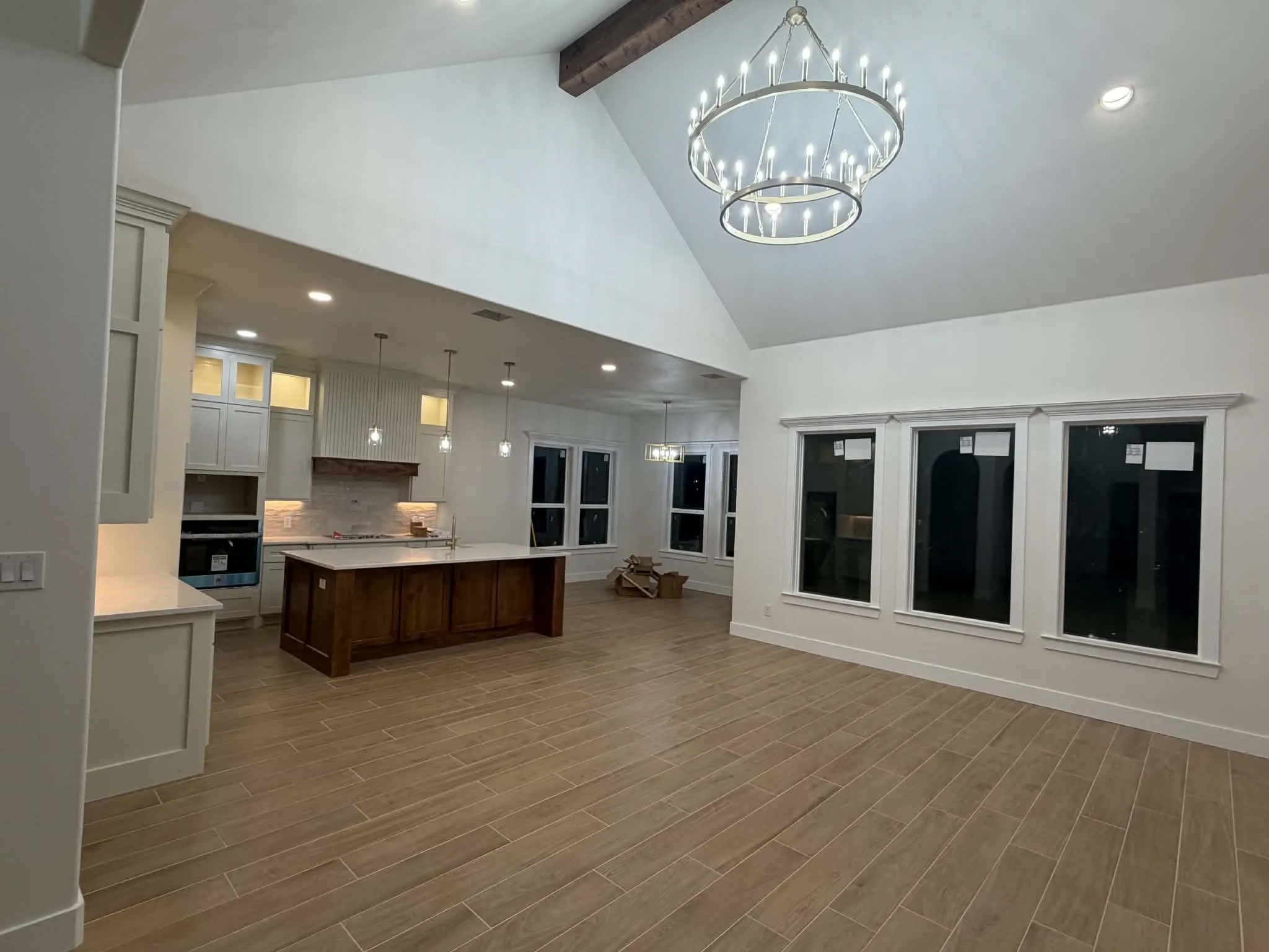 Vaulted ceiling with exposed wood beam, contemporary chandelier, wood-finish flooring, white cabinetry, and a central kitchen island with pendant lighting