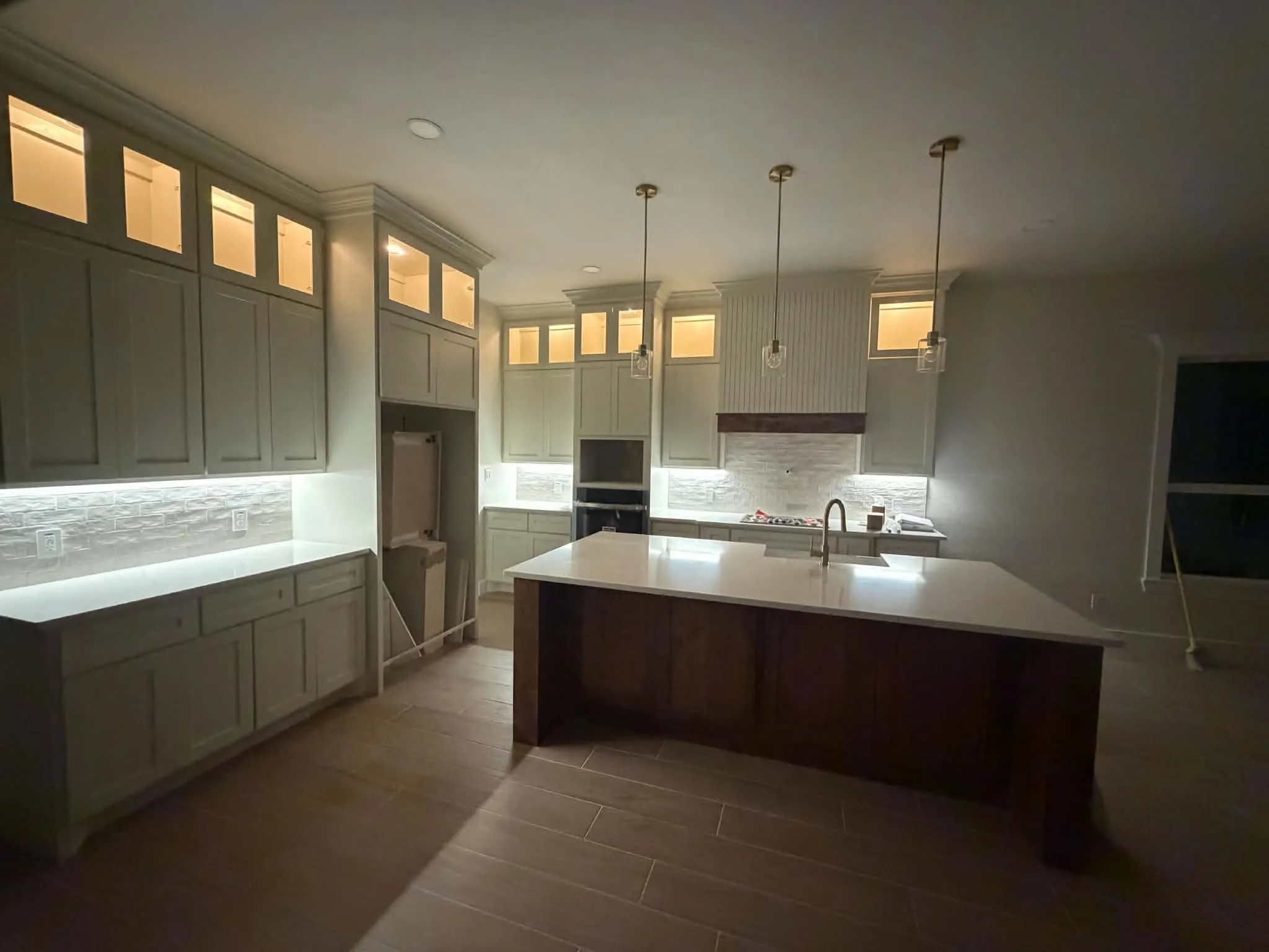 Kitchen featuring a large central island, overhead pendant lighting, under-cabinet lighting, full-height cabinetry, and wood-finish flooring