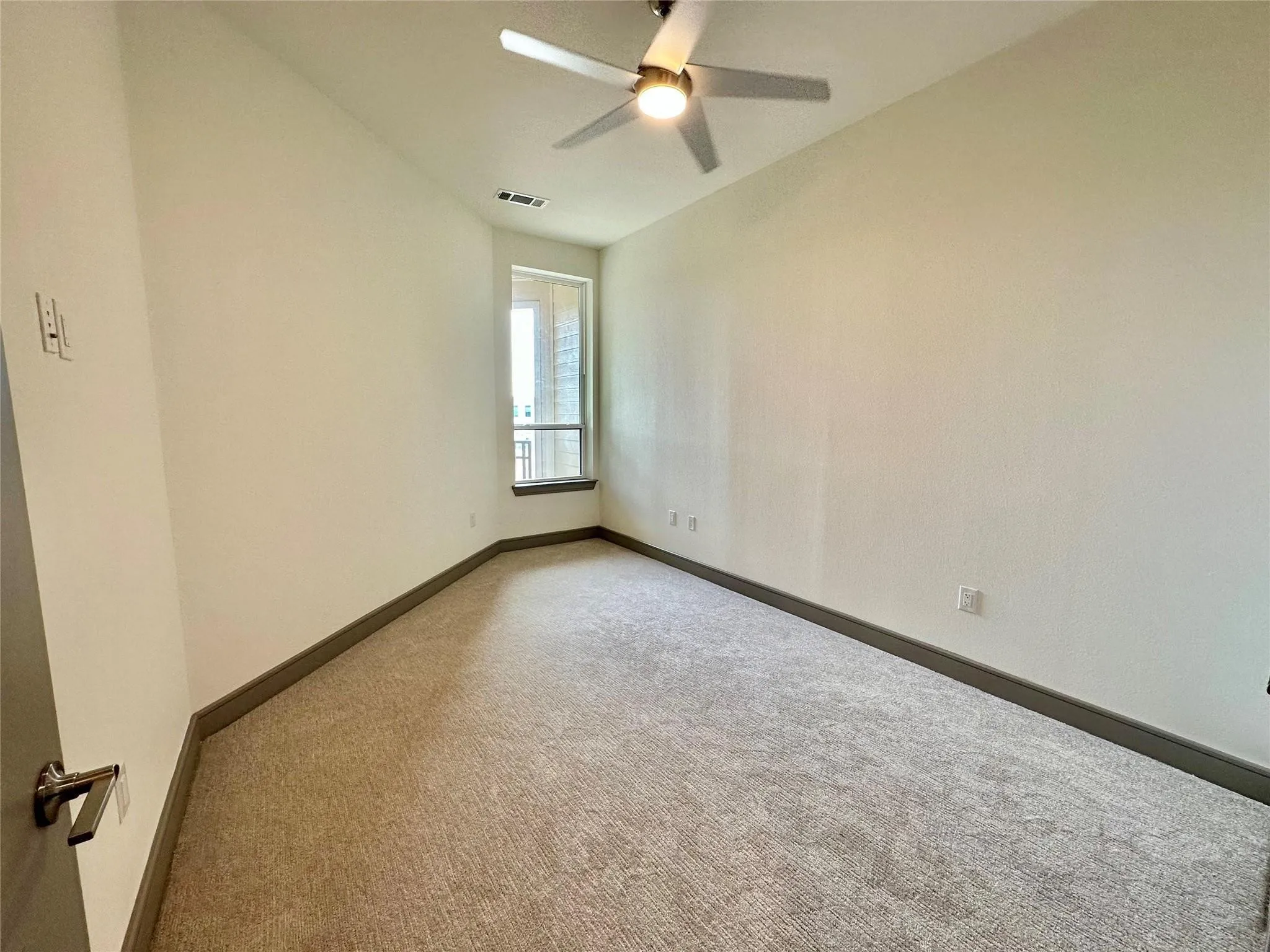 Light-filled room featuring neutral-toned carpet flooring, a window offering exterior views, and a ceiling fan with integrated lighting