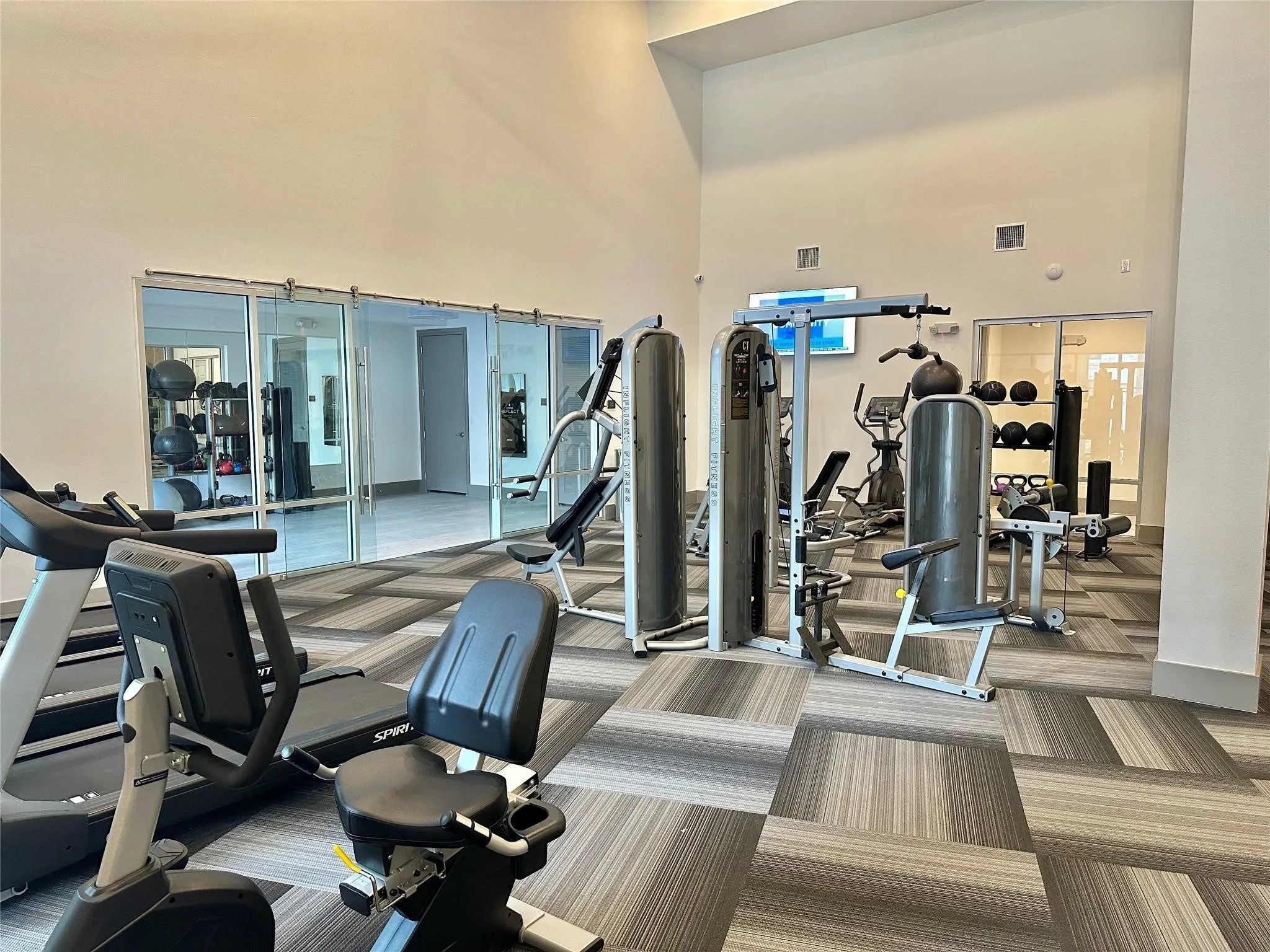 Fitness center with high ceilings, glass partition walls, and patterned carpet