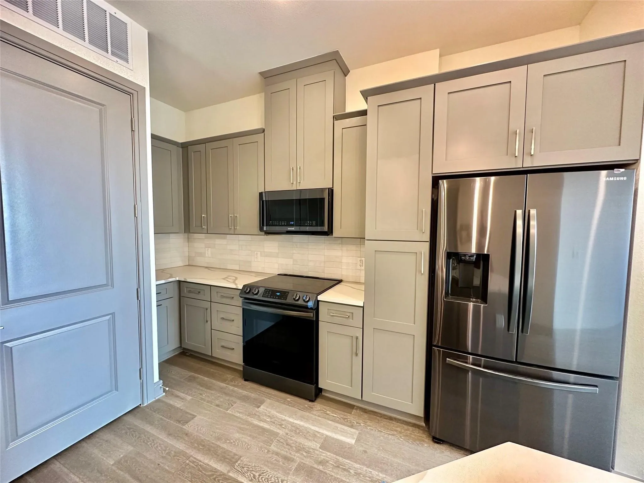 Modern kitchen featuring light gray cabinetry, stainless steel appliances, white subway tile backsplash, light-toned countertops, and wood-finish flooring