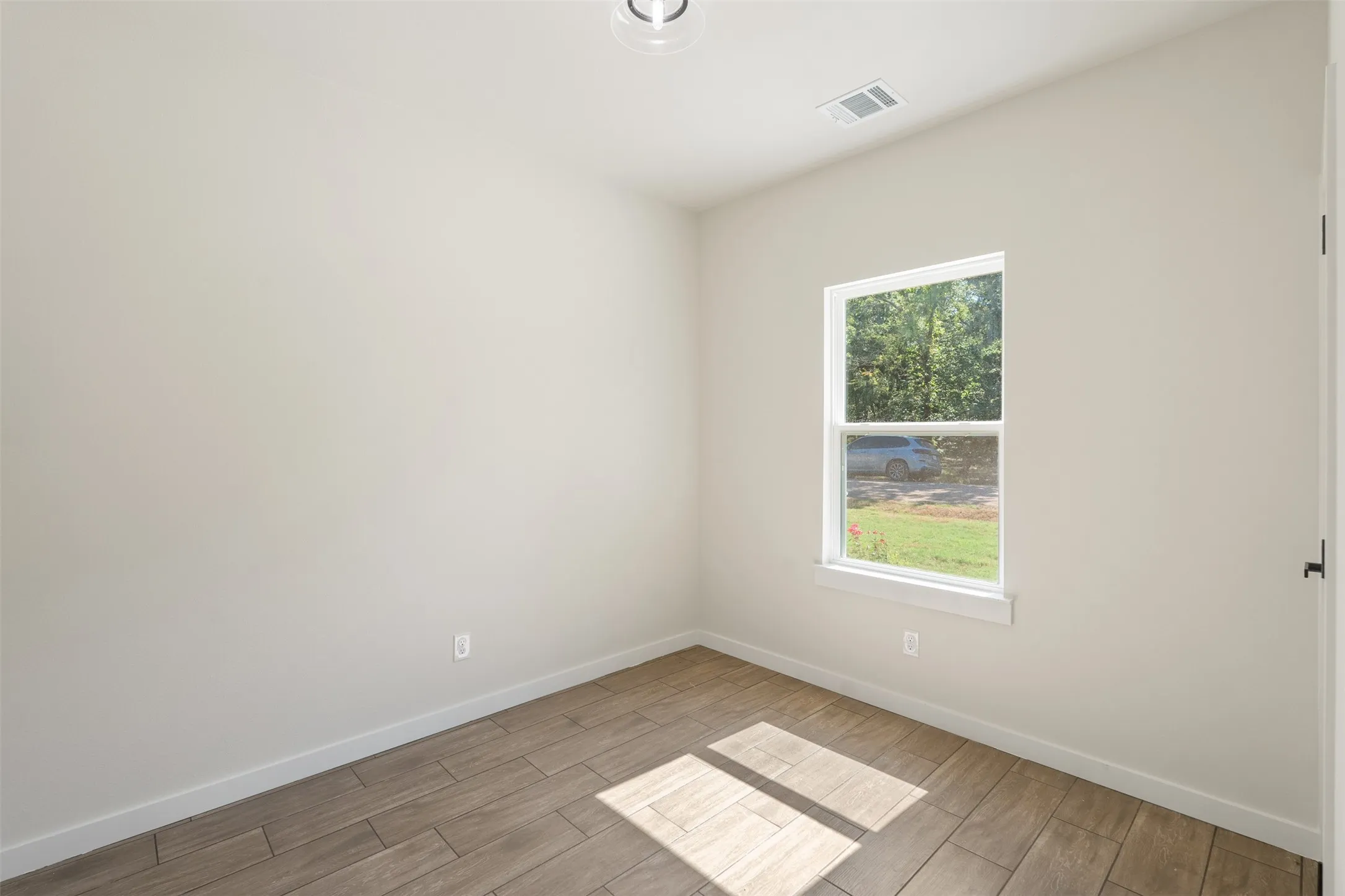 Room featuring light-toned walls, wood-finish flooring, a single double-hung window, and a modern ceiling light fixture