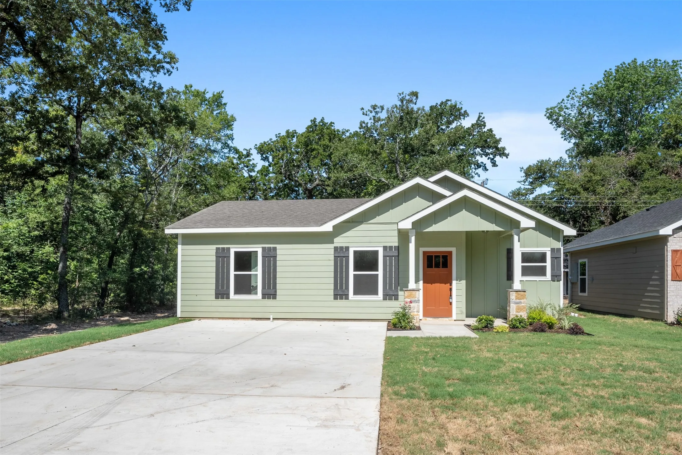 Sage green exterior with white trim, a covered porch, and a bright orange entry door