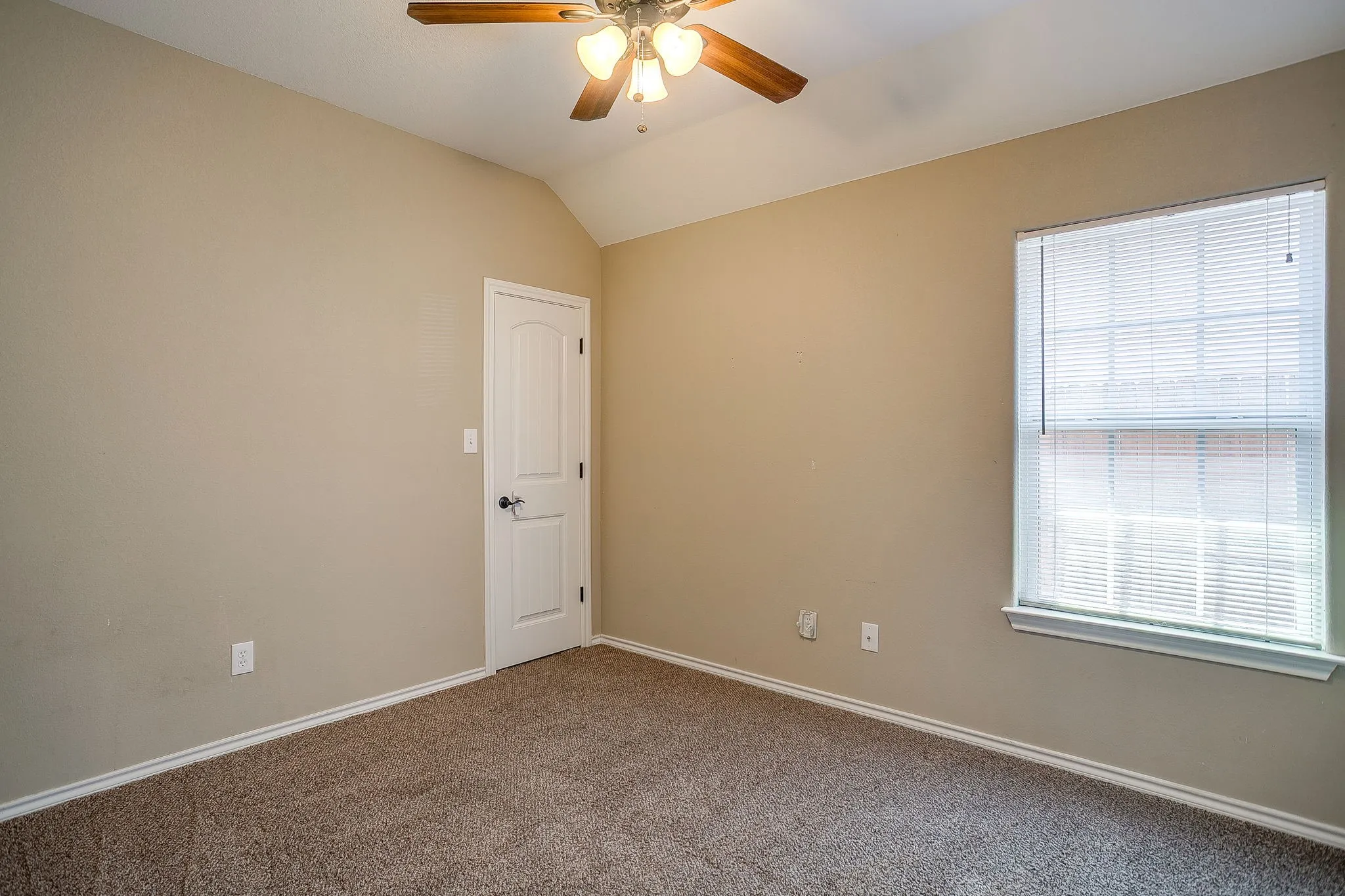 Carpeted room featuring a vaulted ceiling and a wood-finish ceiling fan