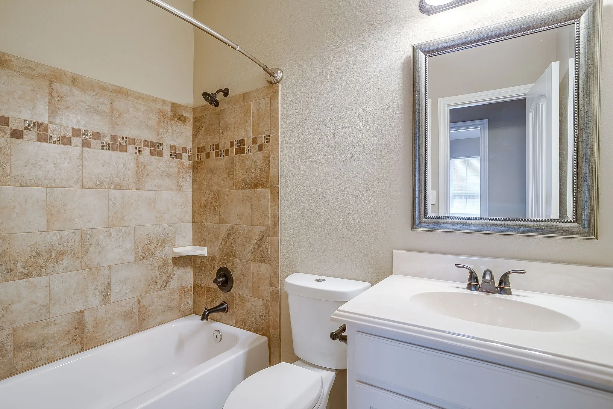 Bathroom featuring a white bathtub, tiled shower surround with decorative accent, white vanity with integrated sink, and an ornate framed mirror