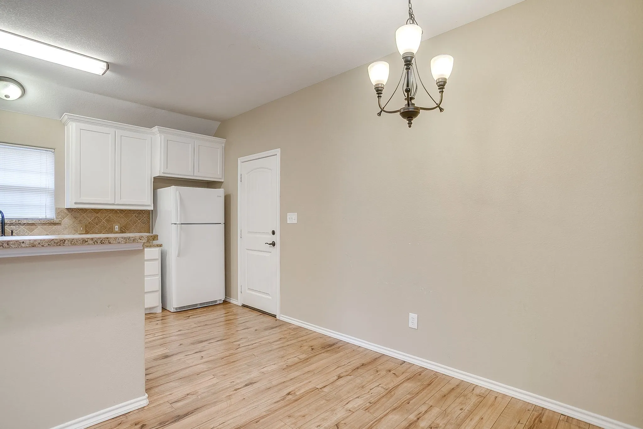 Open-concept dining area featuring wood-finish flooring, a contemporary chandelier, and a neutral wall palette