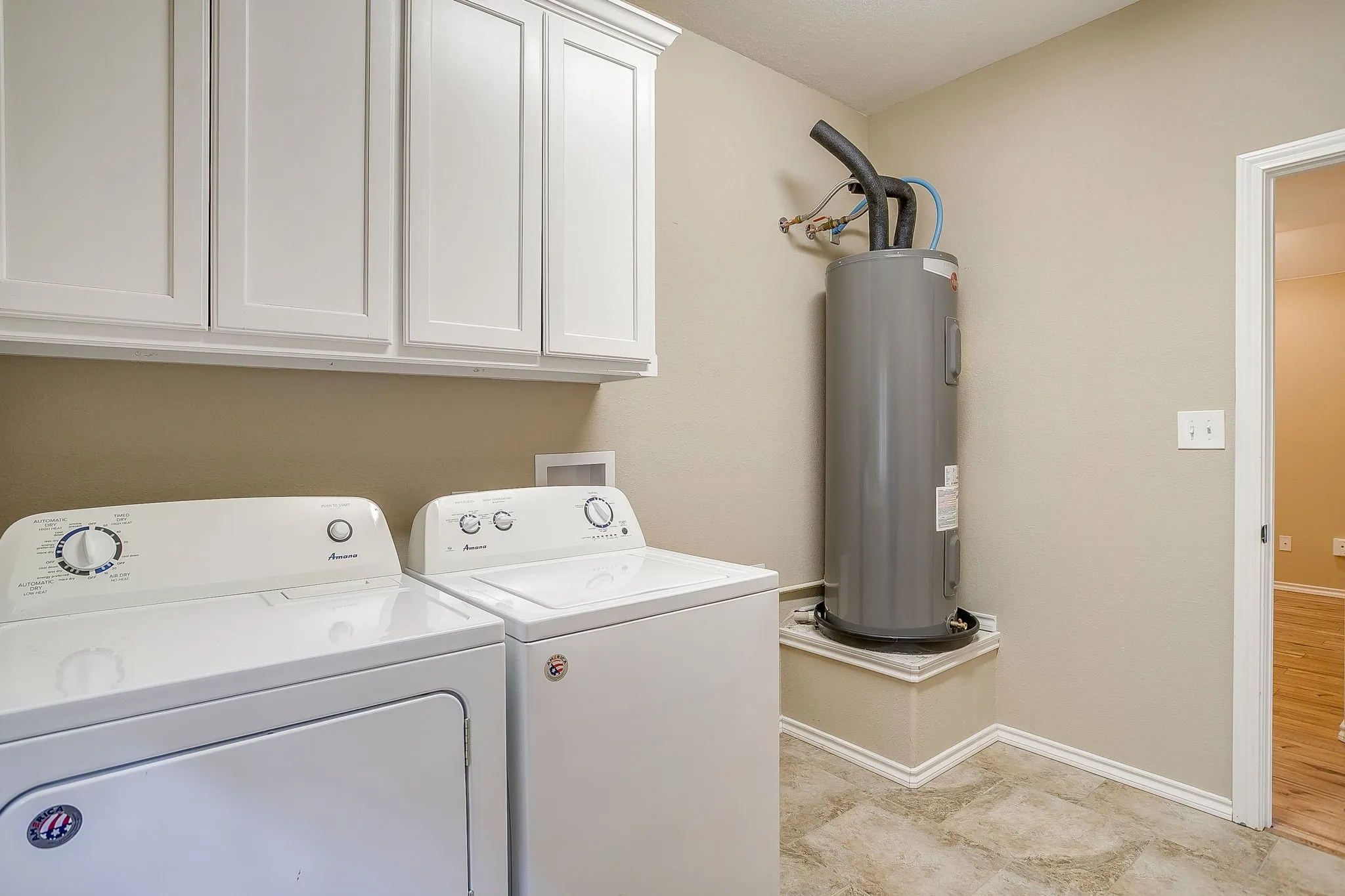 Dedicated utility area featuring overhead white cabinetry, a built-in water heater platform, and neutral-toned wall paint