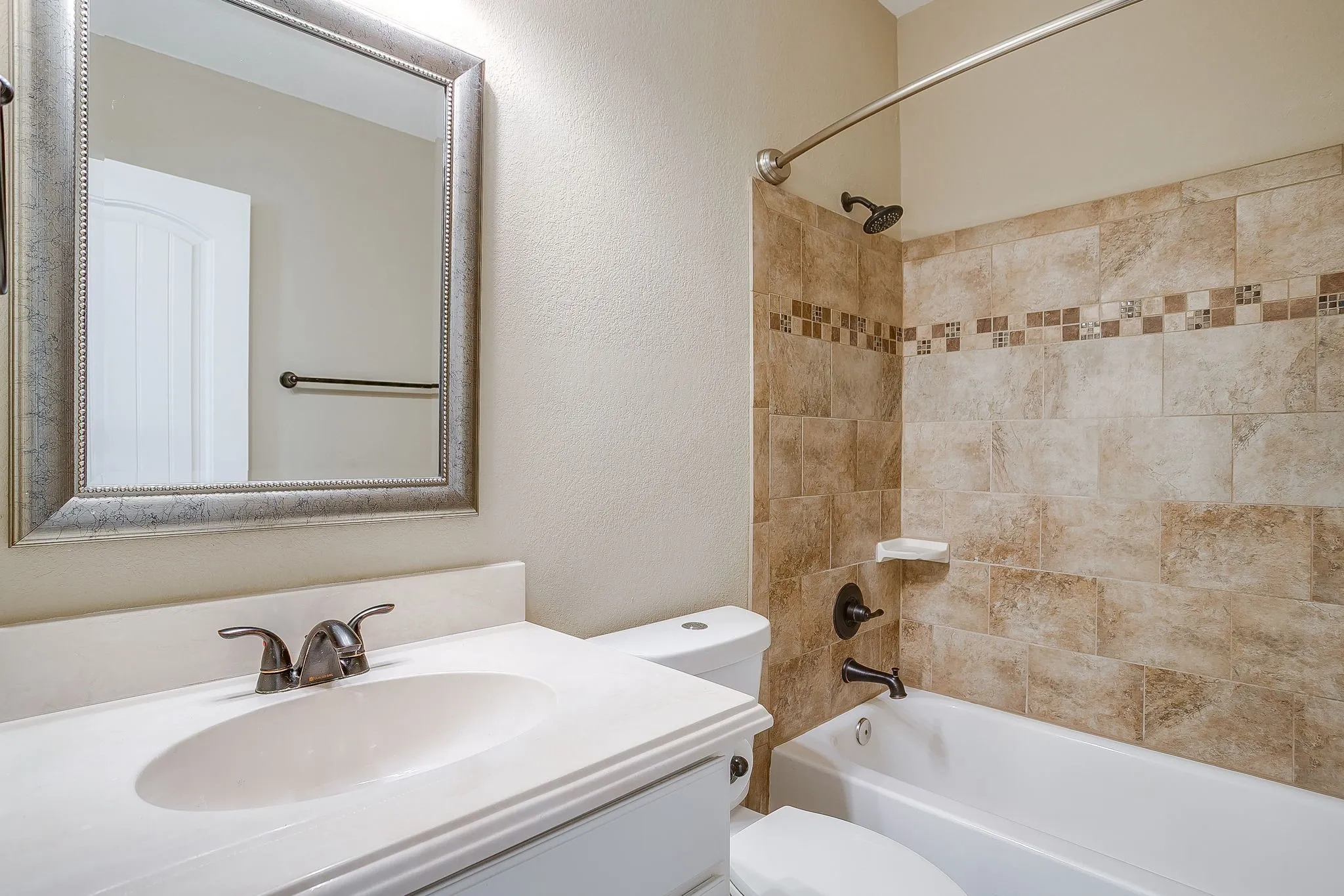 Bathroom featuring a vanity with an integrated sink, a framed mirror, and a bathtub with tile surround