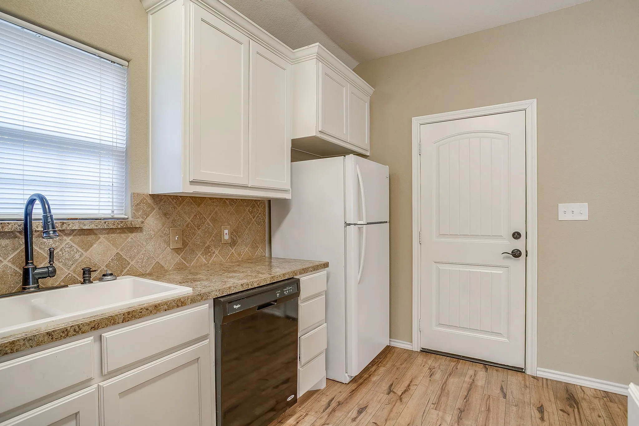 Kitchen featuring wood-finish flooring, white cabinetry, speckled countertops, a tile backsplash, and a white paneled door