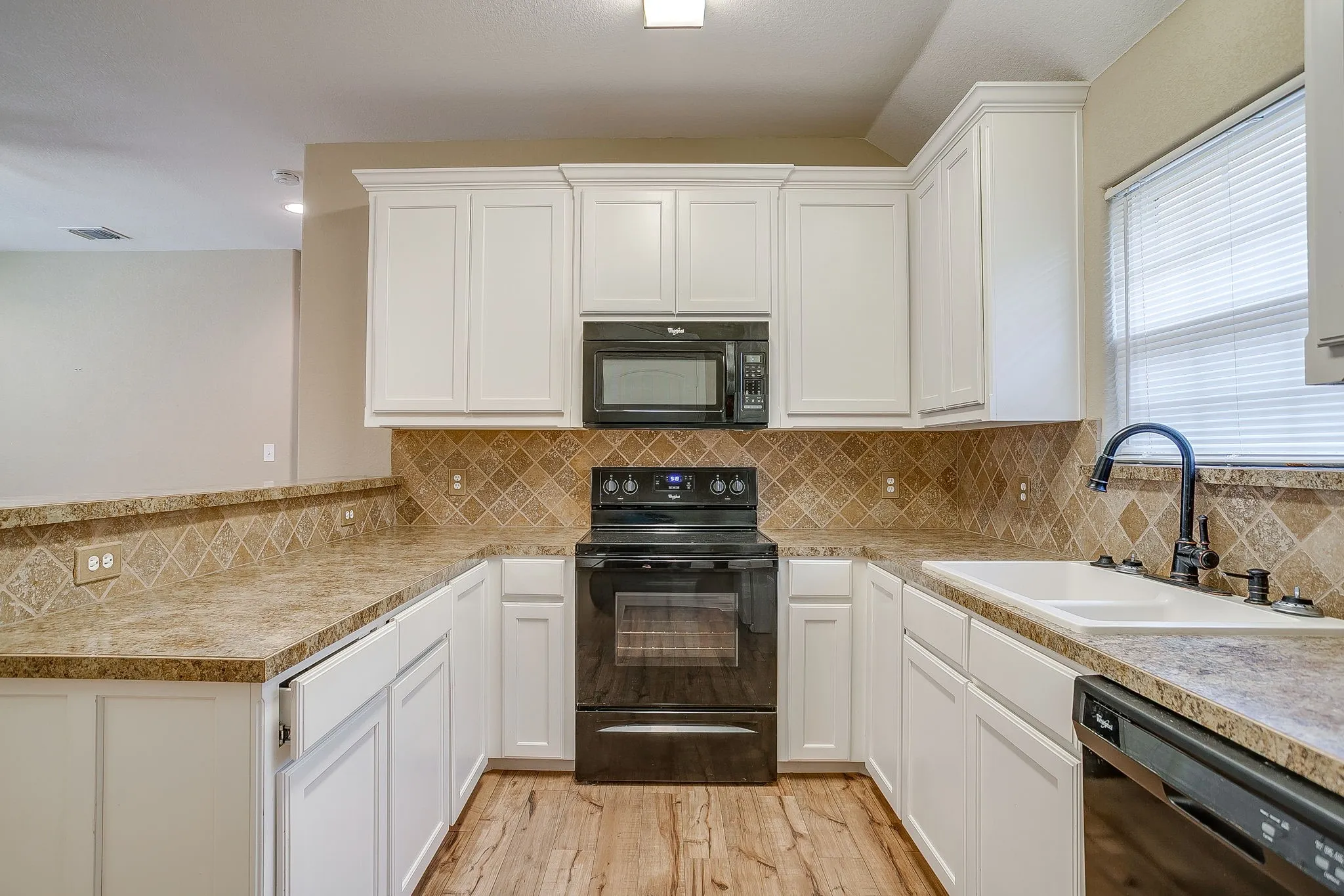 U-shaped kitchen featuring white cabinetry, stone-look countertops, and a patterned tile backsplash