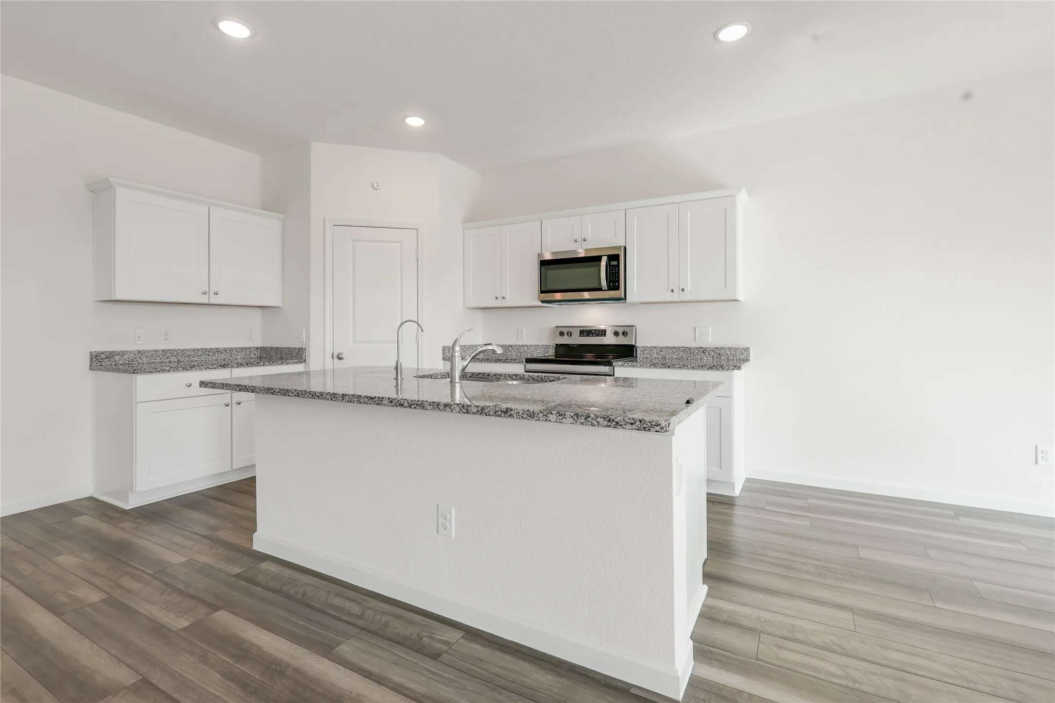 Kitchen featuring an island with a stainless steel faucet, white cabinetry, granite countertops, and wood-finish flooring