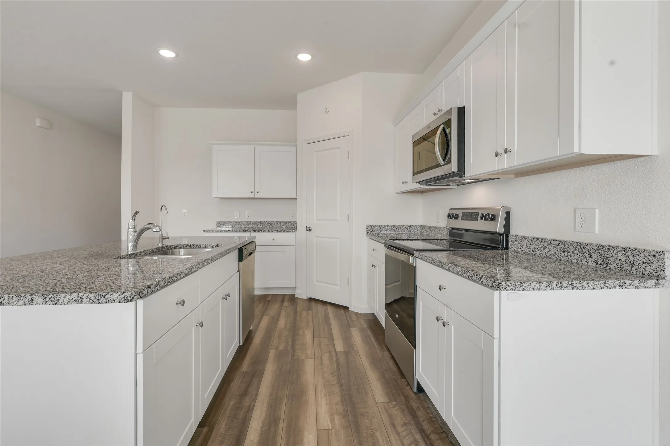 Kitchen featuring water filtration, white cabinetry with silver hardware, granite countertops, stainless steel appliances, and wood-finish flooring