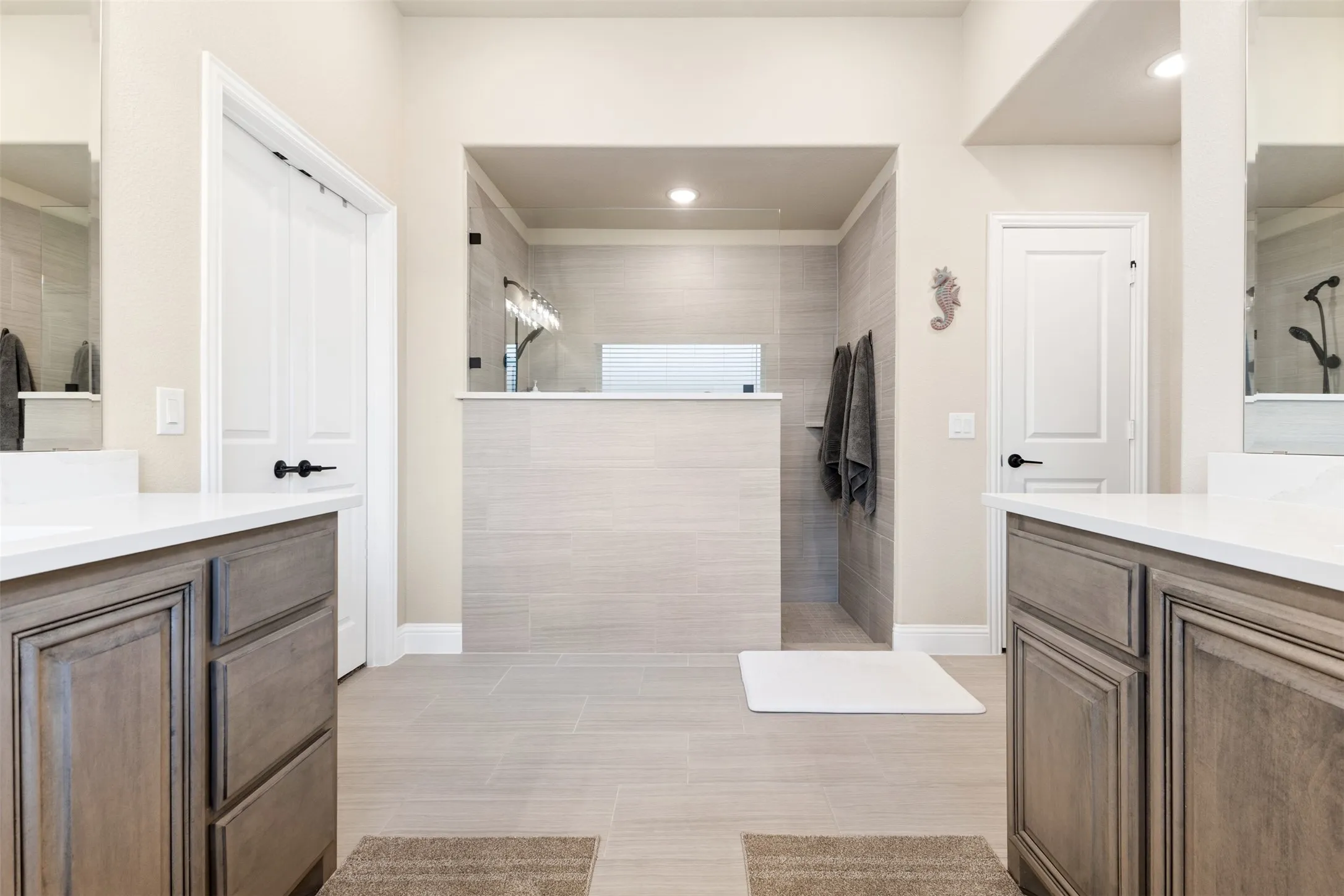Spacious bathroom featuring a walk-in shower with light-toned tile, dual vanity cabinets with stone countertops, and recessed lighting