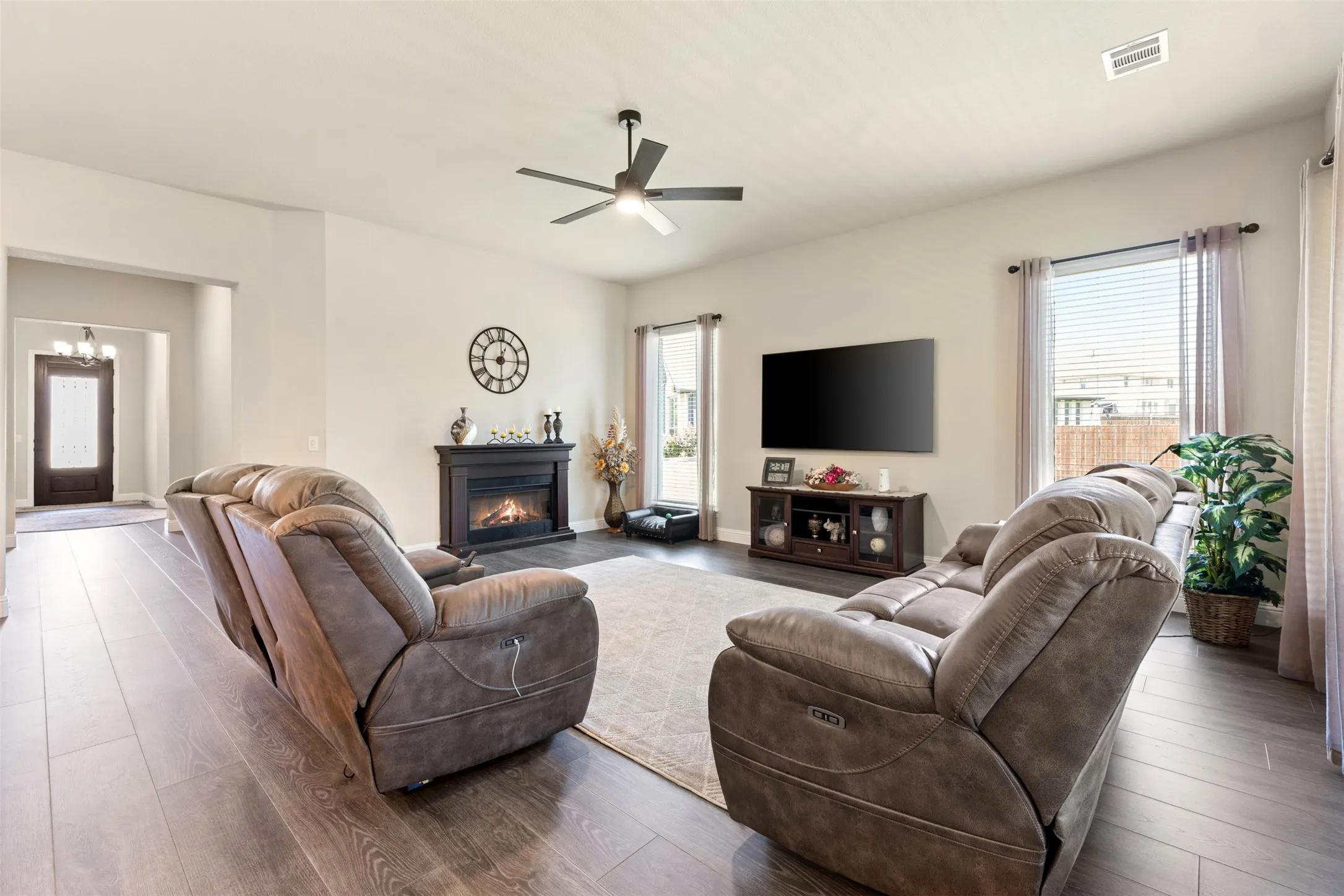 Spacious living area featuring wood-finish flooring, an electric fireplace with a dark mantel, and a ceiling fan with integrated lighting