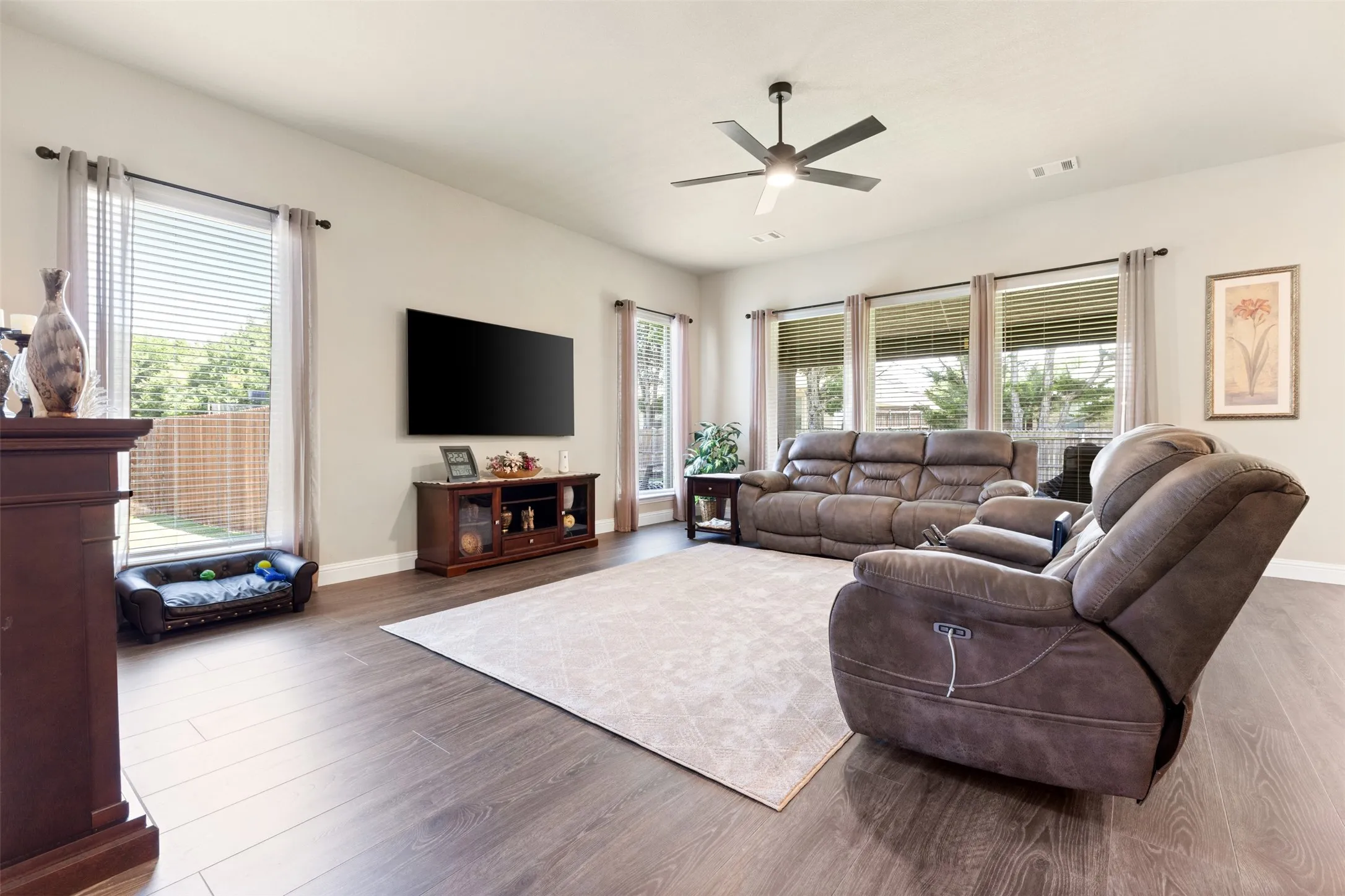 Spacious living area featuring wood-finish flooring, light neutral wall tones, and multiple large windows with blinds