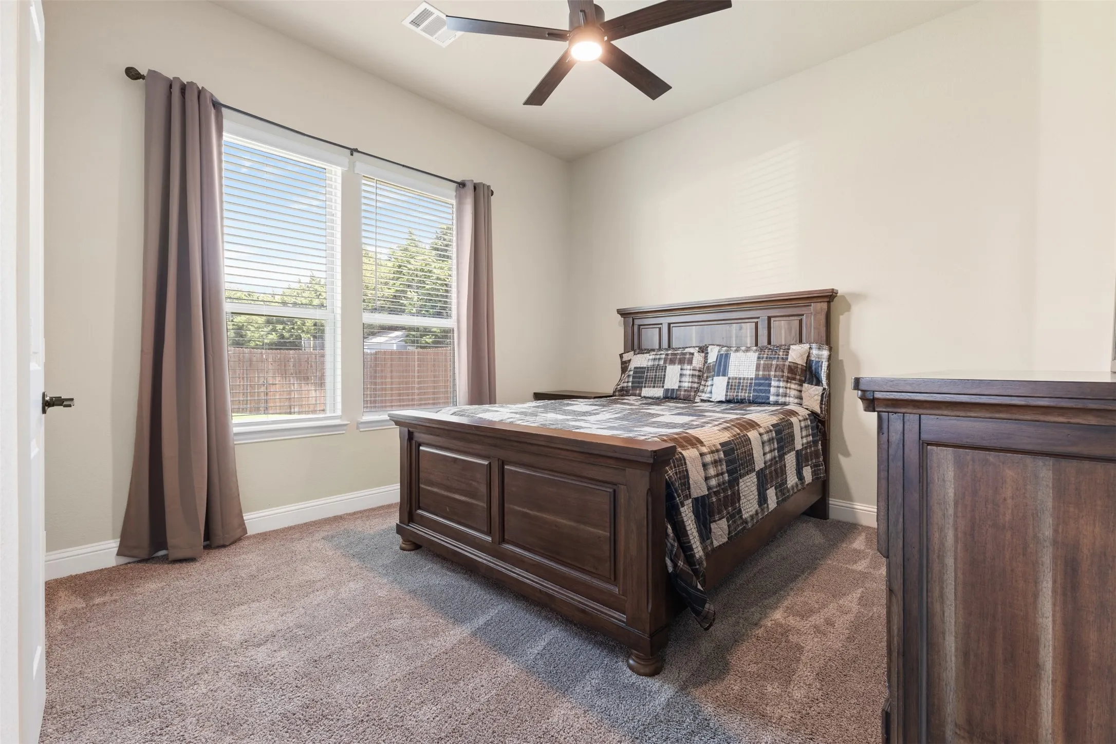 Carpeted room featuring a ceiling fan with integrated lighting, two double-hung windows with blinds, and neutral wall paint