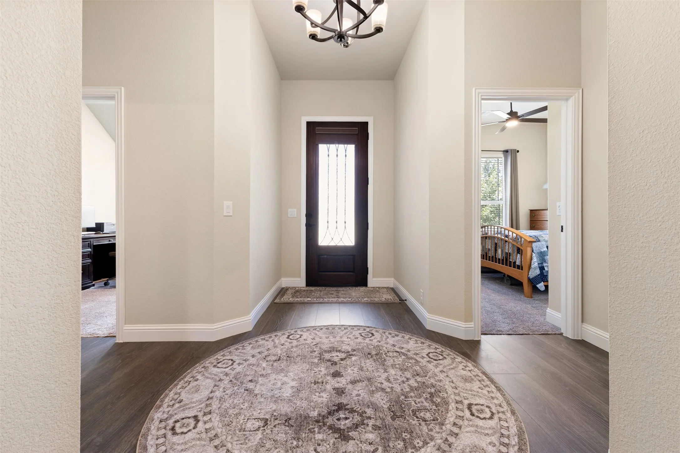 Inviting foyer featuring wood-finish flooring, a dark-paneled door with decorative glass, and a traditional ceiling light fixture