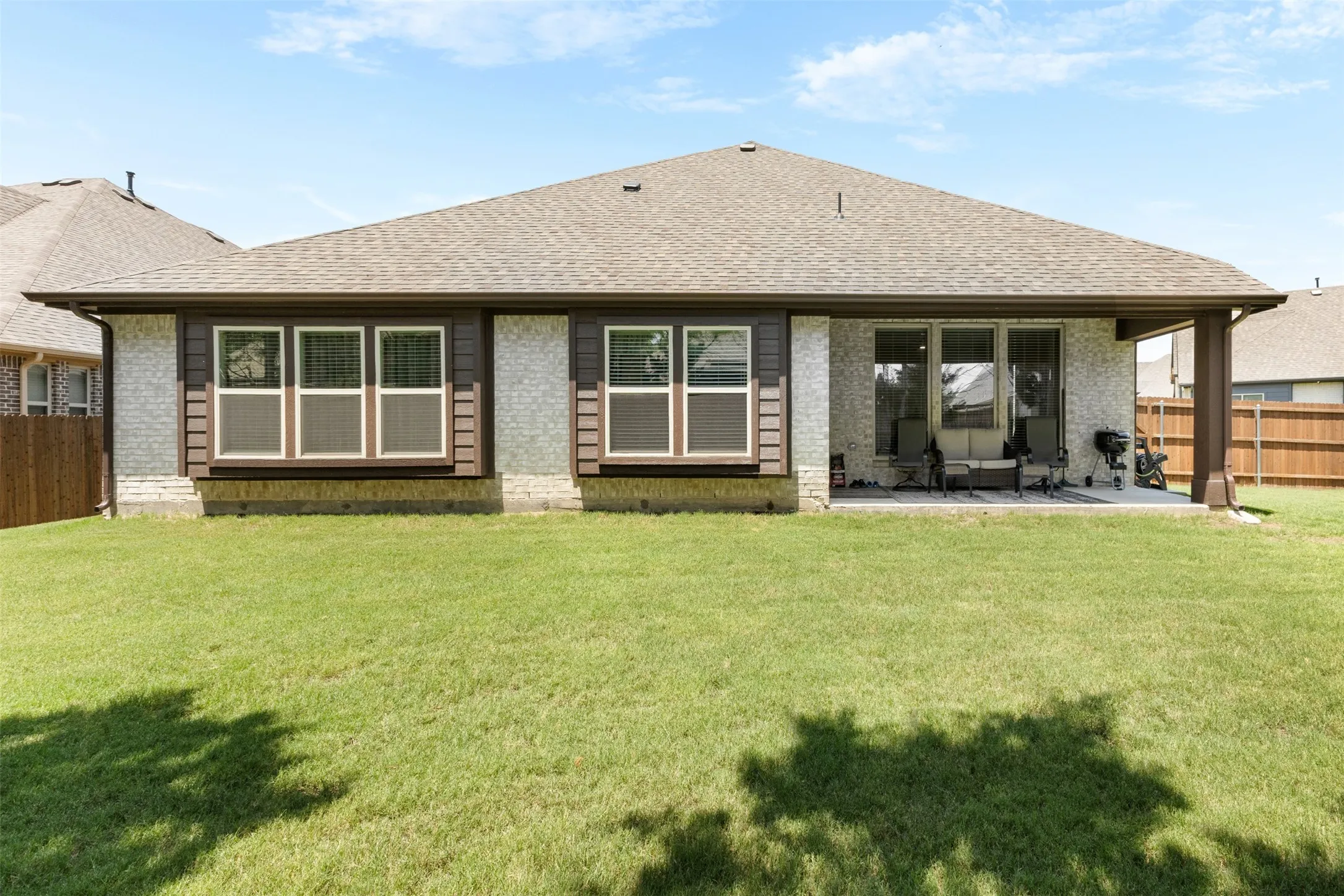 Rear exterior featuring a covered patio, expansive lawn, and partial privacy fencing