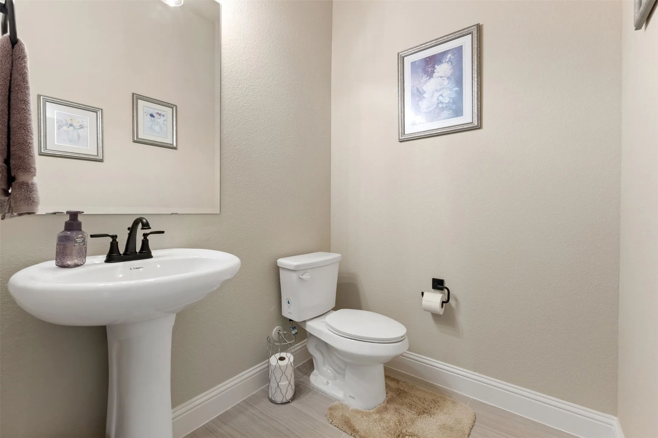 Pedestal sink with a matte black faucet, wall-mounted mirror, and light wood-finish flooring